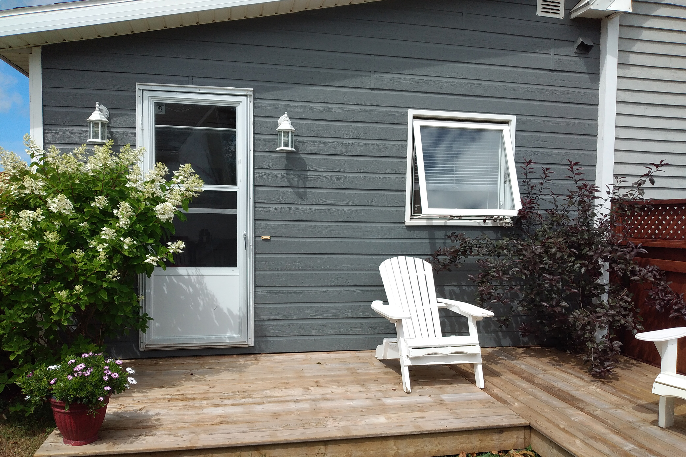 Gray house with white front door and adirondack chair sitting outside.