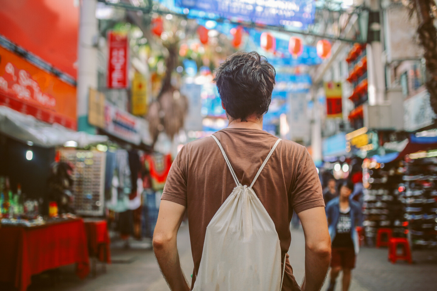 Rear view image of a young man, solo traveler, walking in the Chinatown district of Kuala Lumpur, Malaysia. He is wearing a white rucksack, enjoying walking and shopping in Malaysia capital.