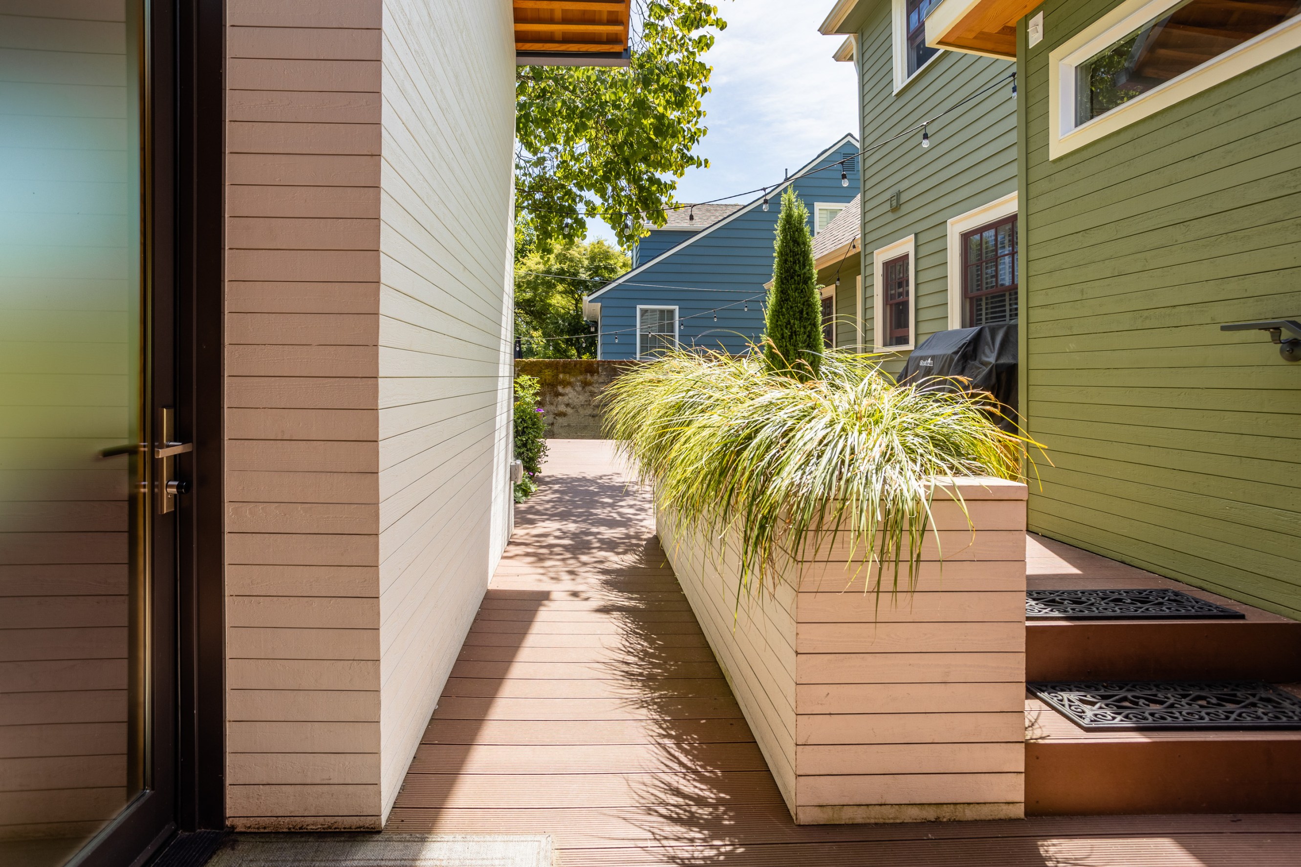 A wheelchair accessible ramp leading towards the driveway alongside a long planter with hanging grass.