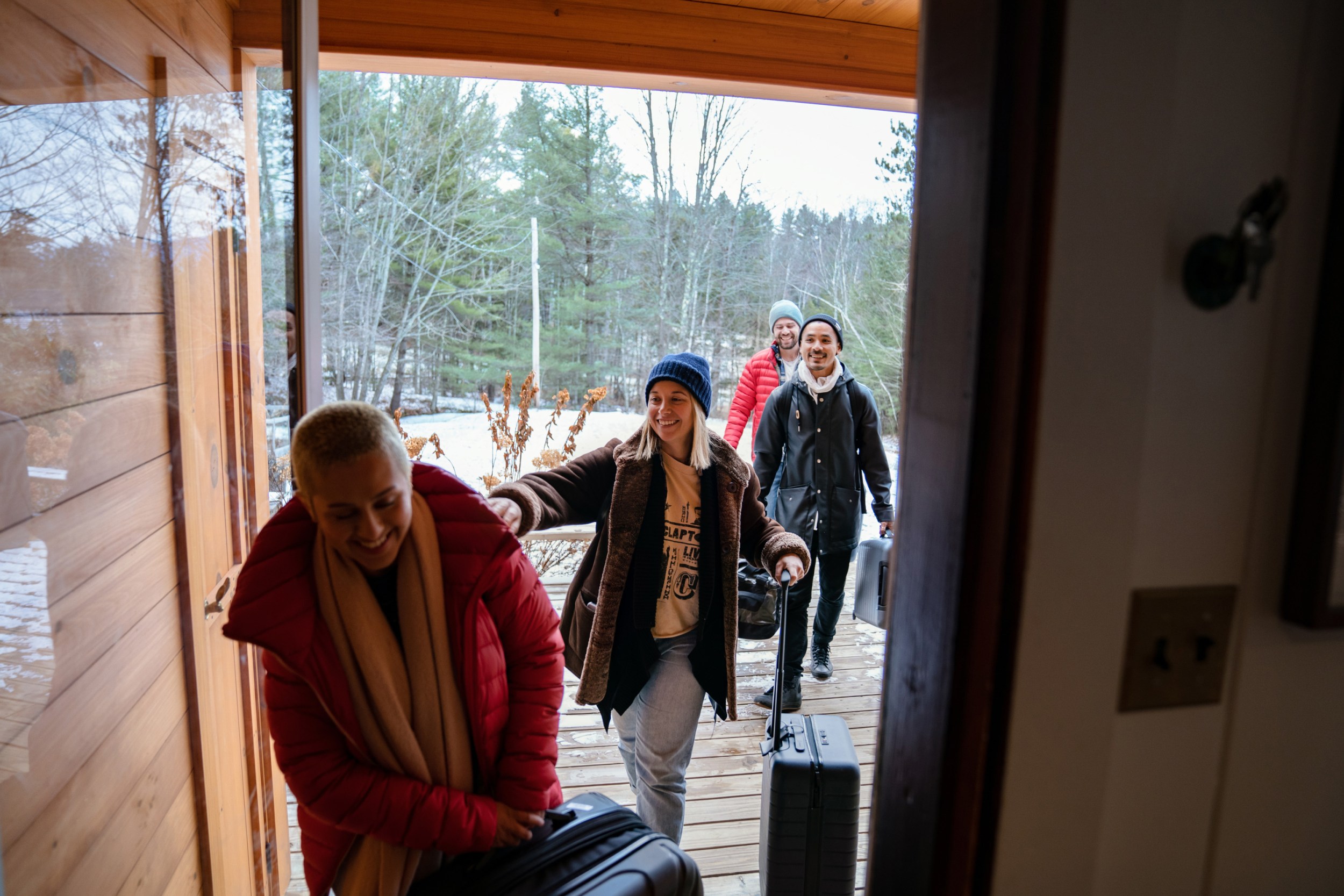 A group of people bundled up in winter apparel walking through an Airbnb entryway with a snowy landscape in the background.