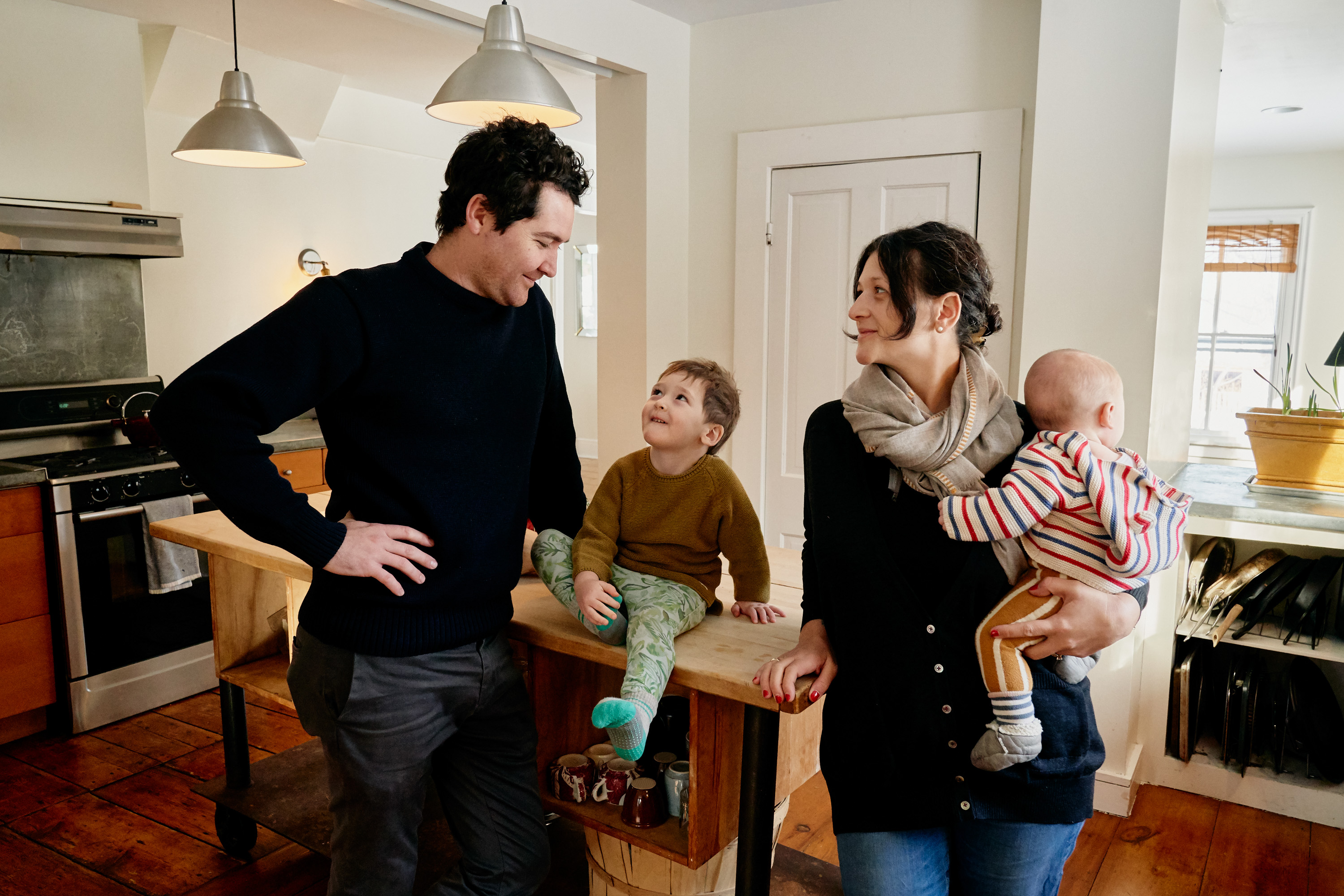 Young family of four, including a dad, mother, a young son and baby are gathered in their Airbnb listing kitchen.