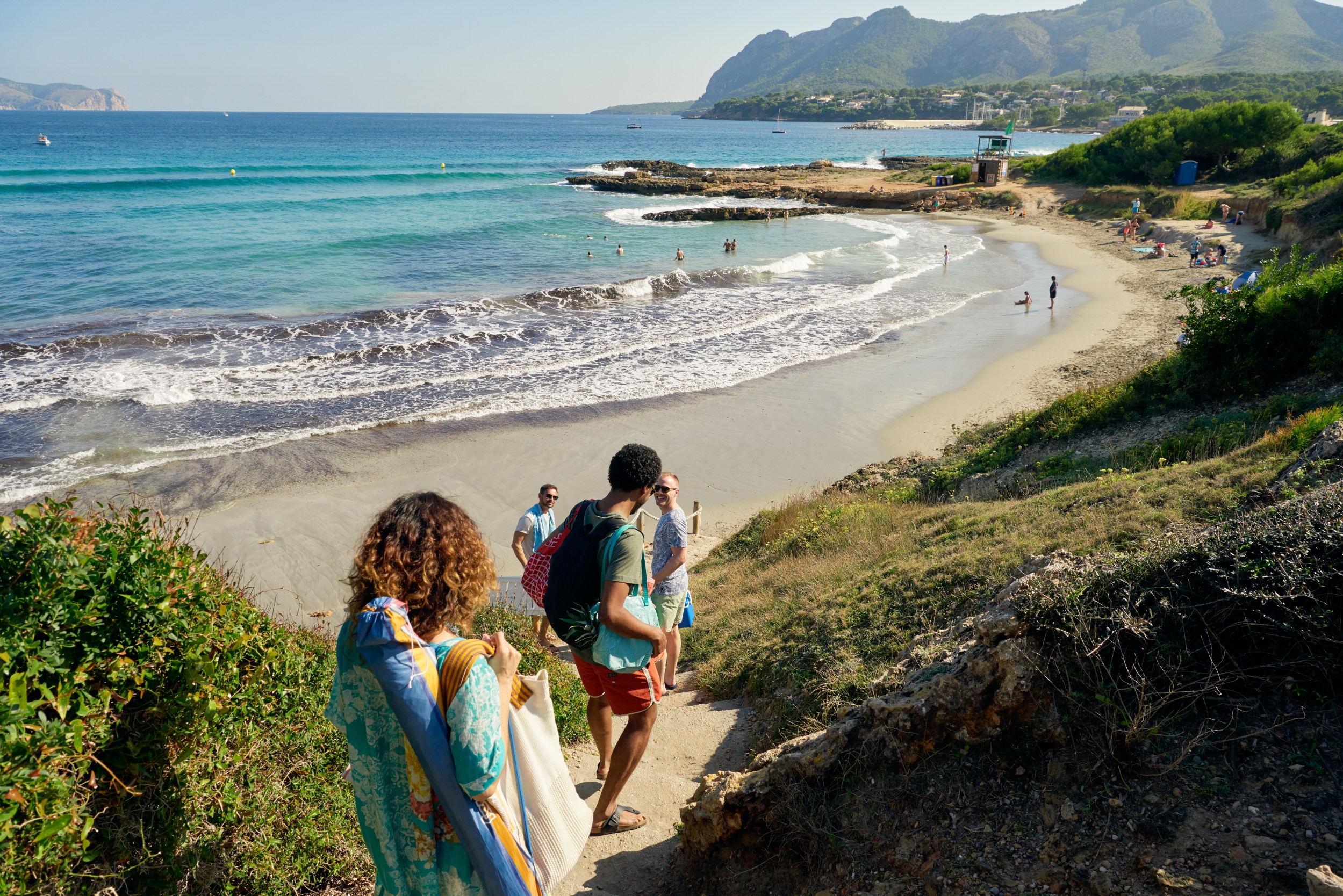 Group of travelers walking down a sandy path to an untouched beach.