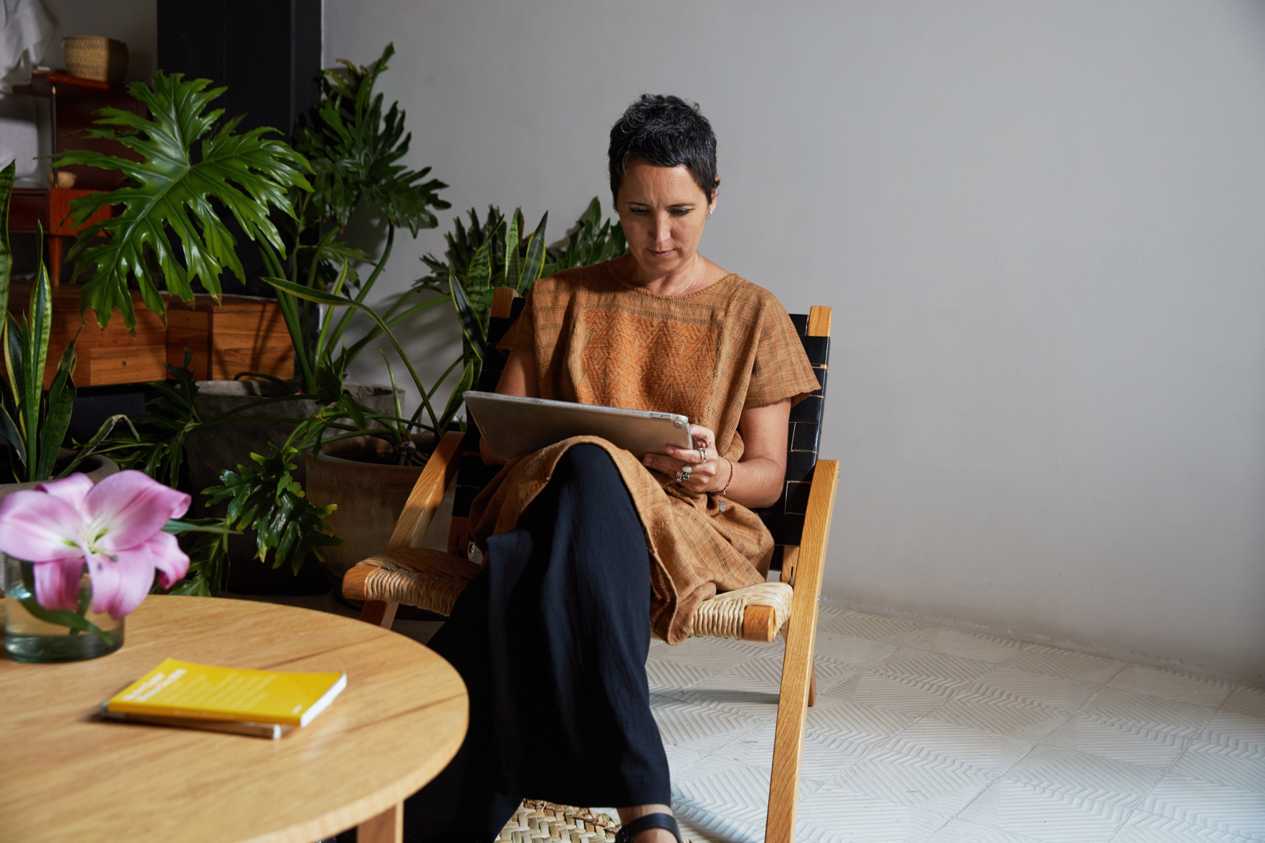 Woman sitting in a chair looking at an iPad with a plant behind her.