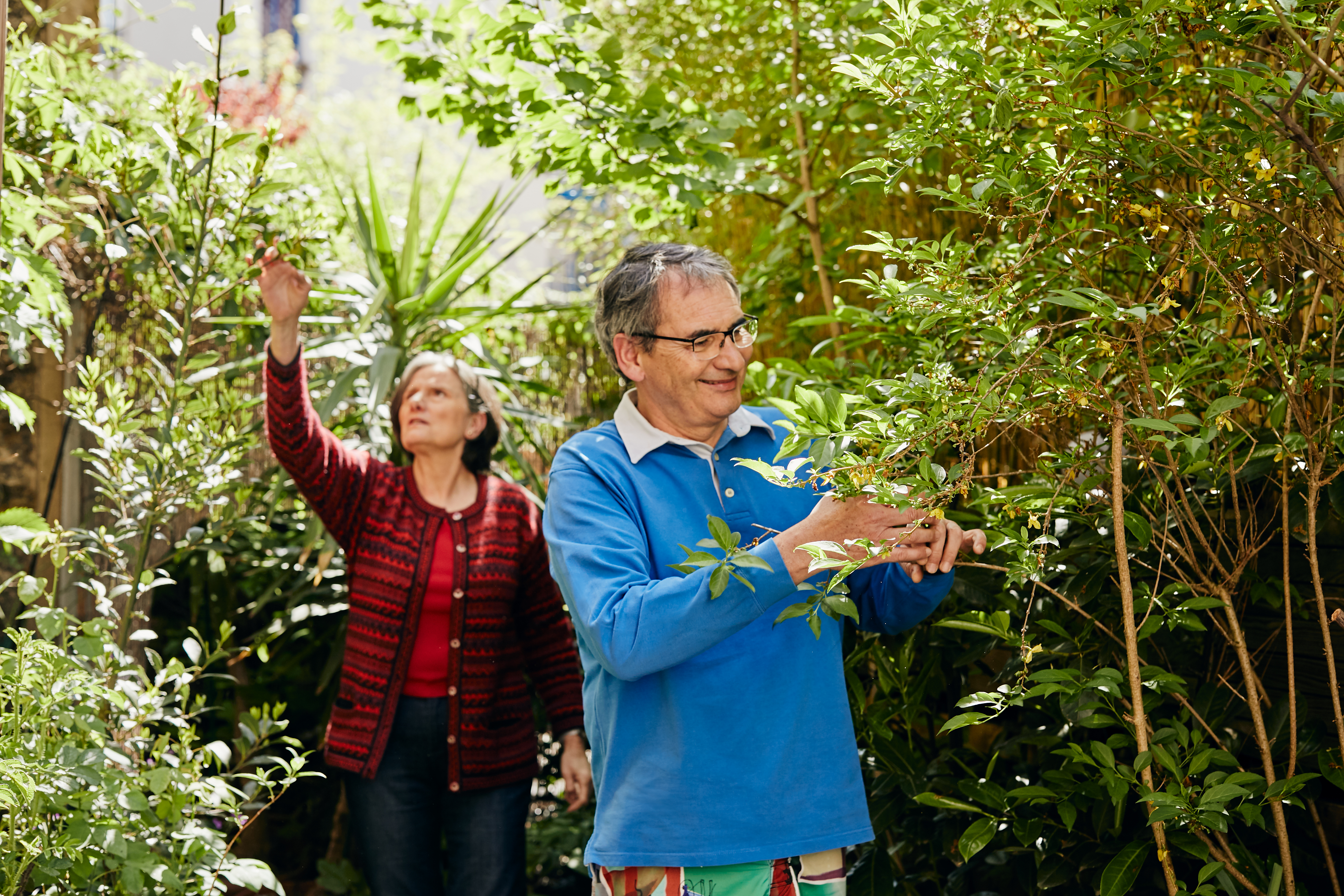 A woman and smiling man touch plants in a garden