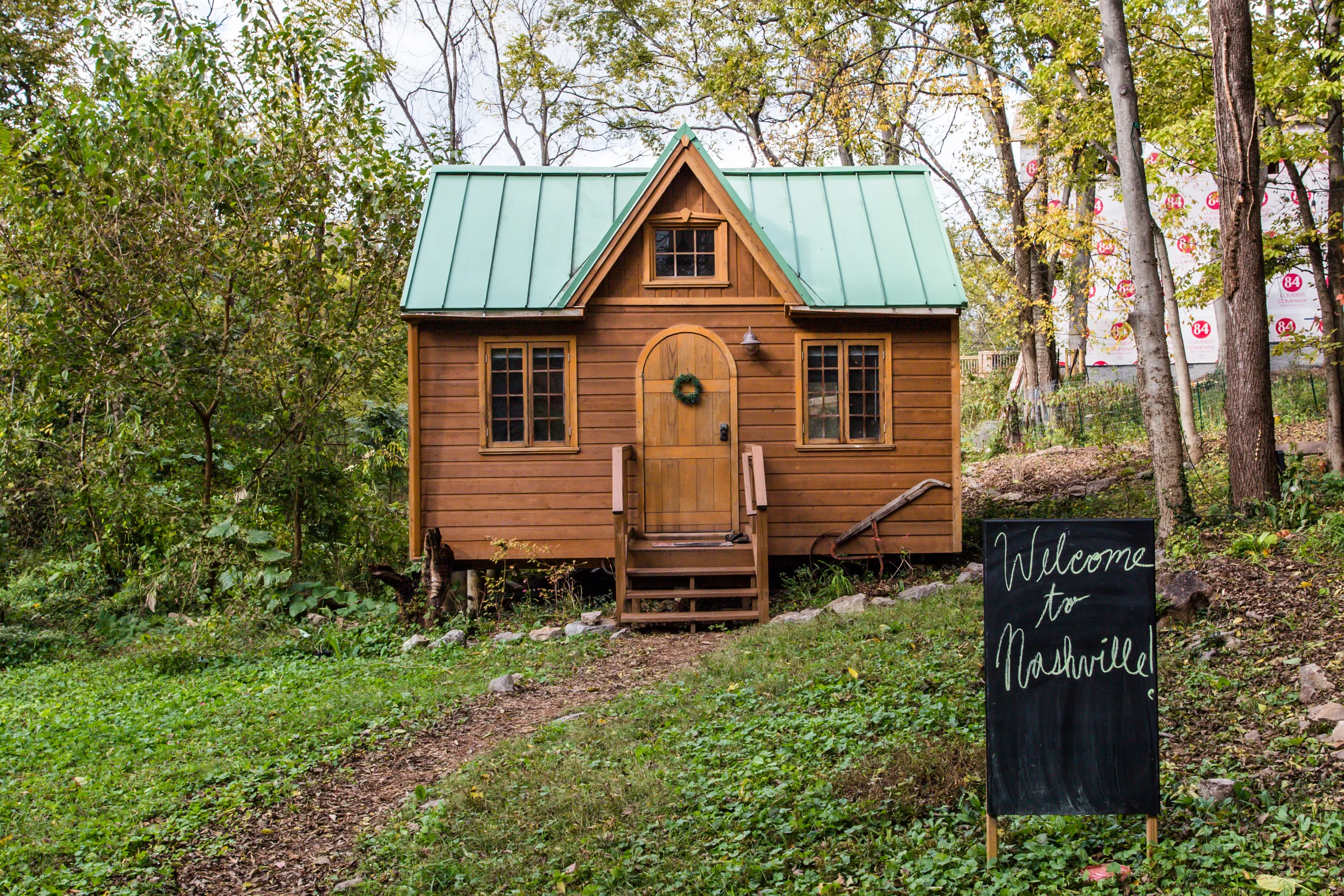 A small brown cabin with a turquoise roof surrounded by trees with a small chalkboard sign in front of the house with the text “Welcome to Nashville”