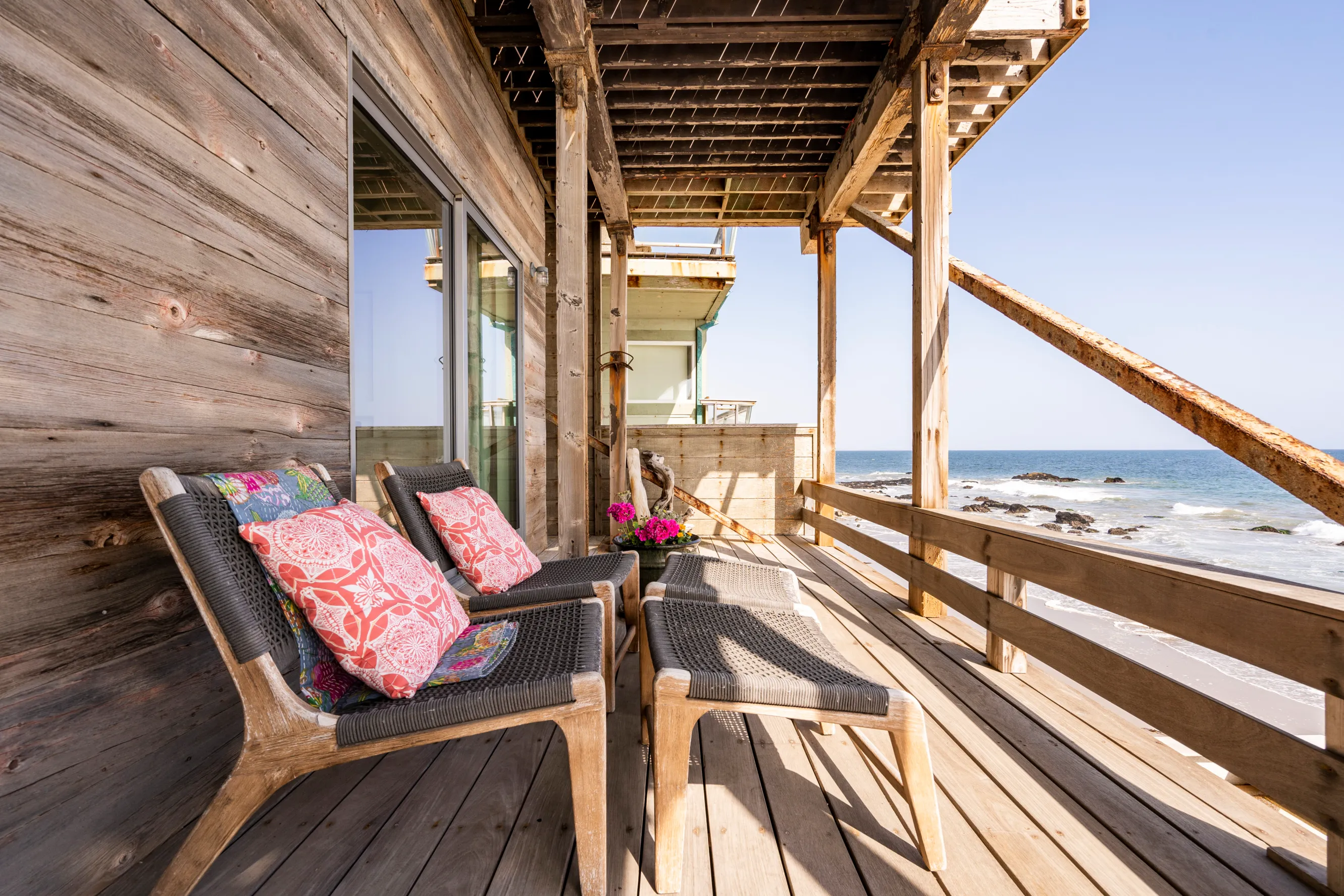 Wooden porch with two bench chairs perched in front of a railing looking over a sandy beach and the ocean