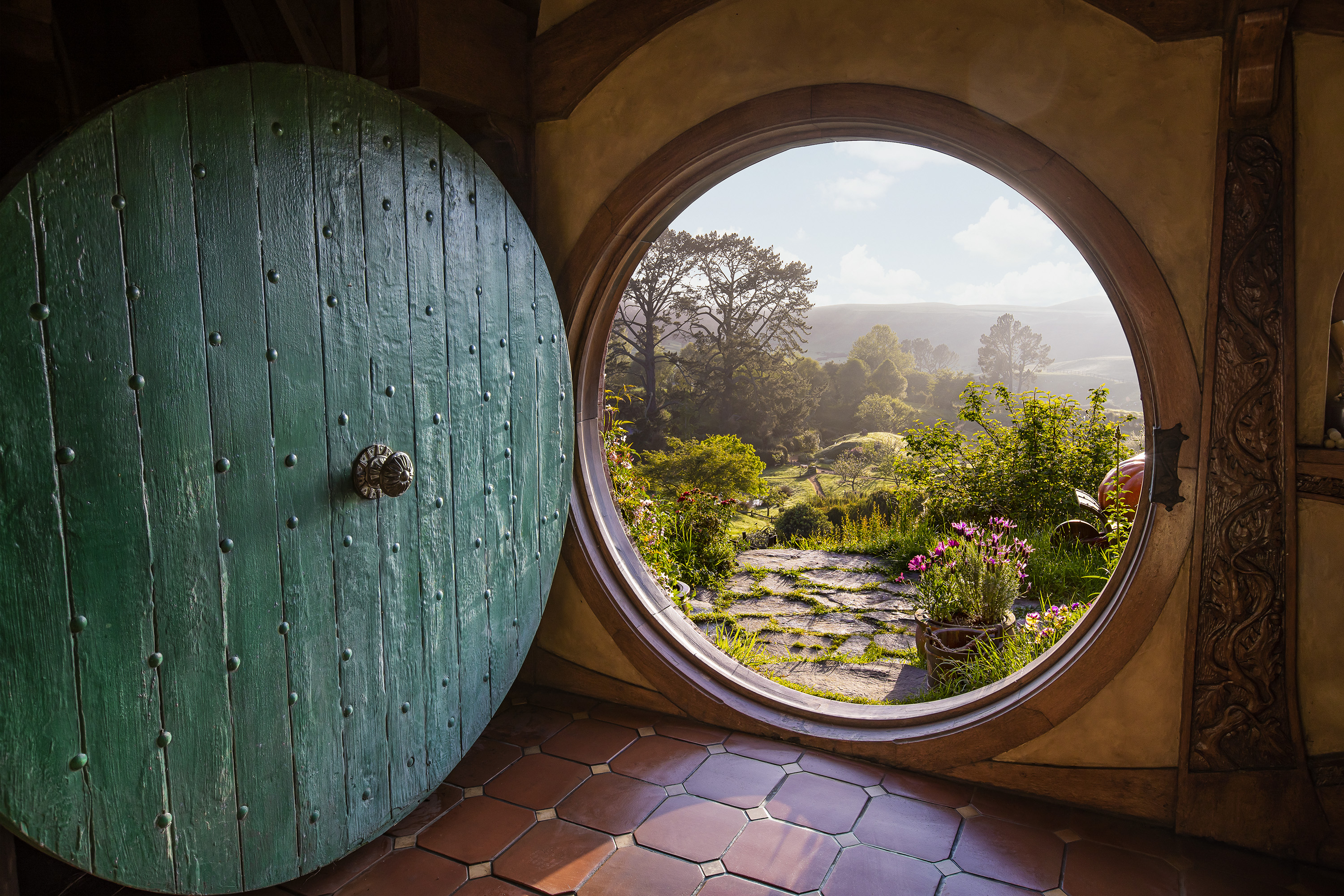 View from the Hobbit Hole entryway into the stay. Green circular door opens up to see lush green fields and trees outside the home.