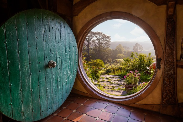 View from the Hobbit Hole entryway into the stay. Green circular door opens up to see lush green fields and trees outside the home.