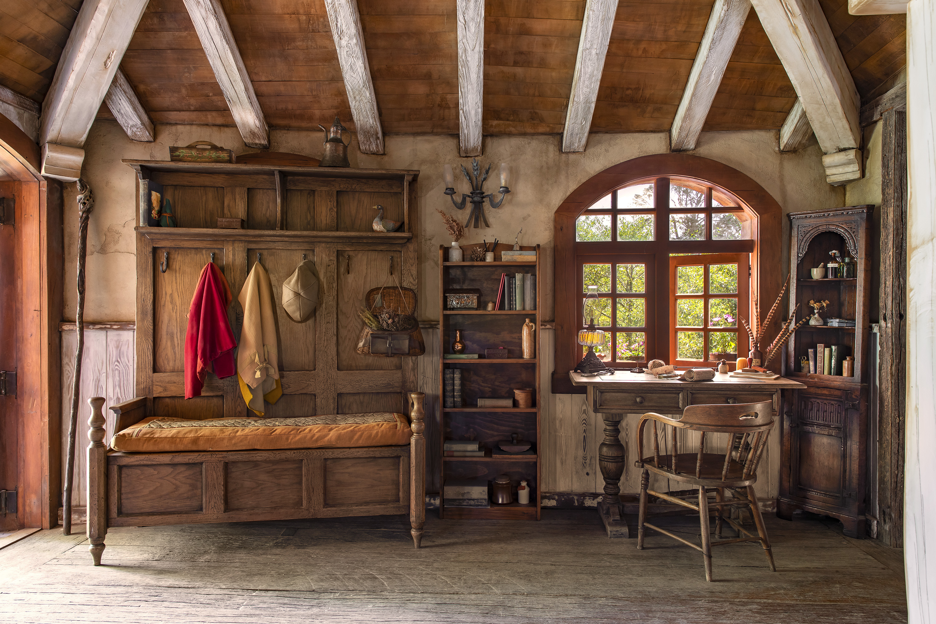 A desk nook complete with a row of coat hangers and a comfortable bench alongside a wooden bookshelf. To the right of the bookshelf is a writer's desk with a quill, paper manuscript and ink ready for any guest's writing leisure.