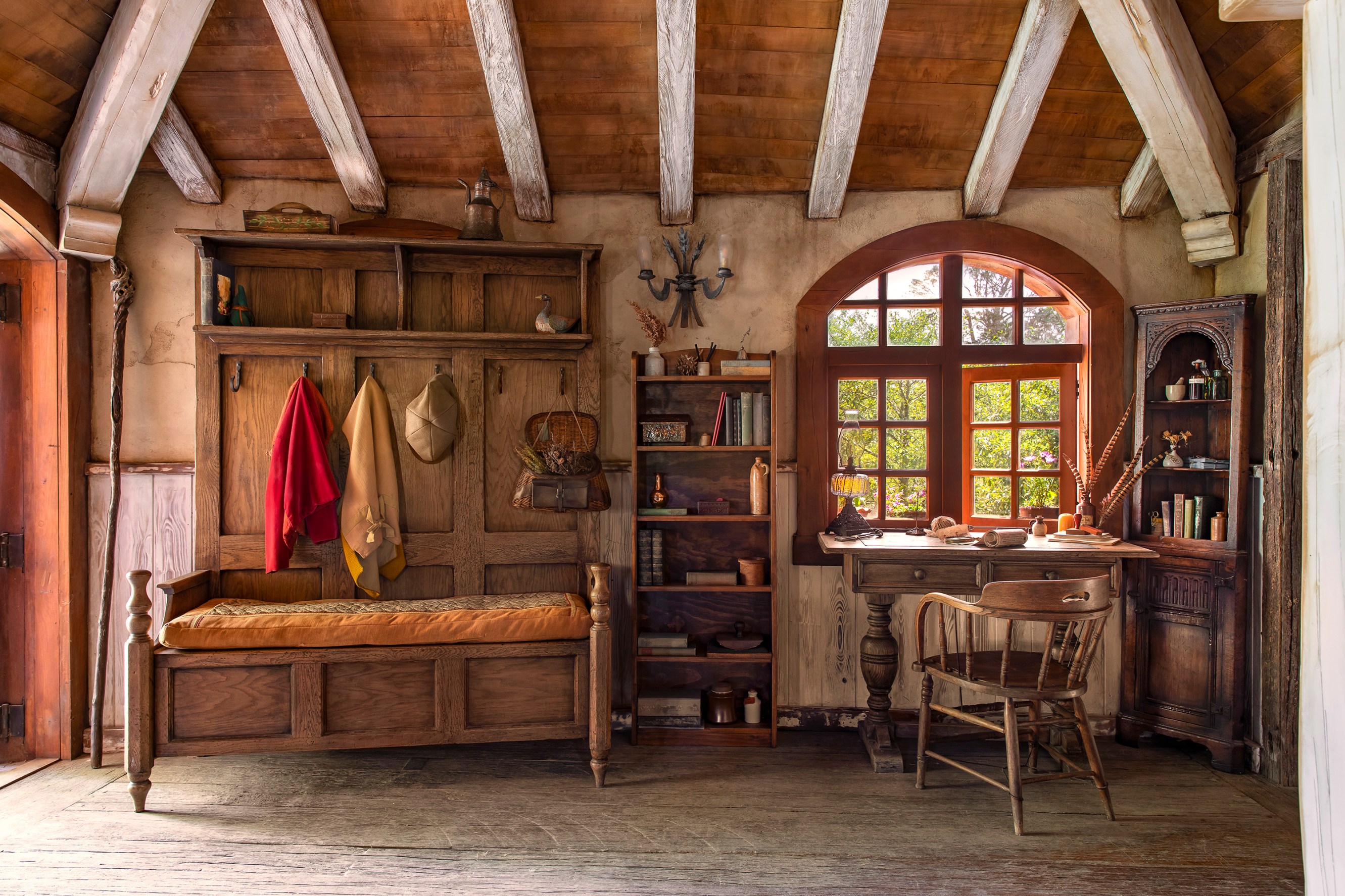 A desk nook complete with a row of coat hangers and a comfortable bench alongside a wooden bookshelf. To the right of the bookshelf is a writer's desk with a quill, paper manuscript and ink ready for any guest's writing leisure.