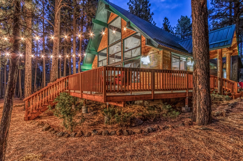Cabin with a wrap around deck in the forrest with twinkle lights hanging from the trees
