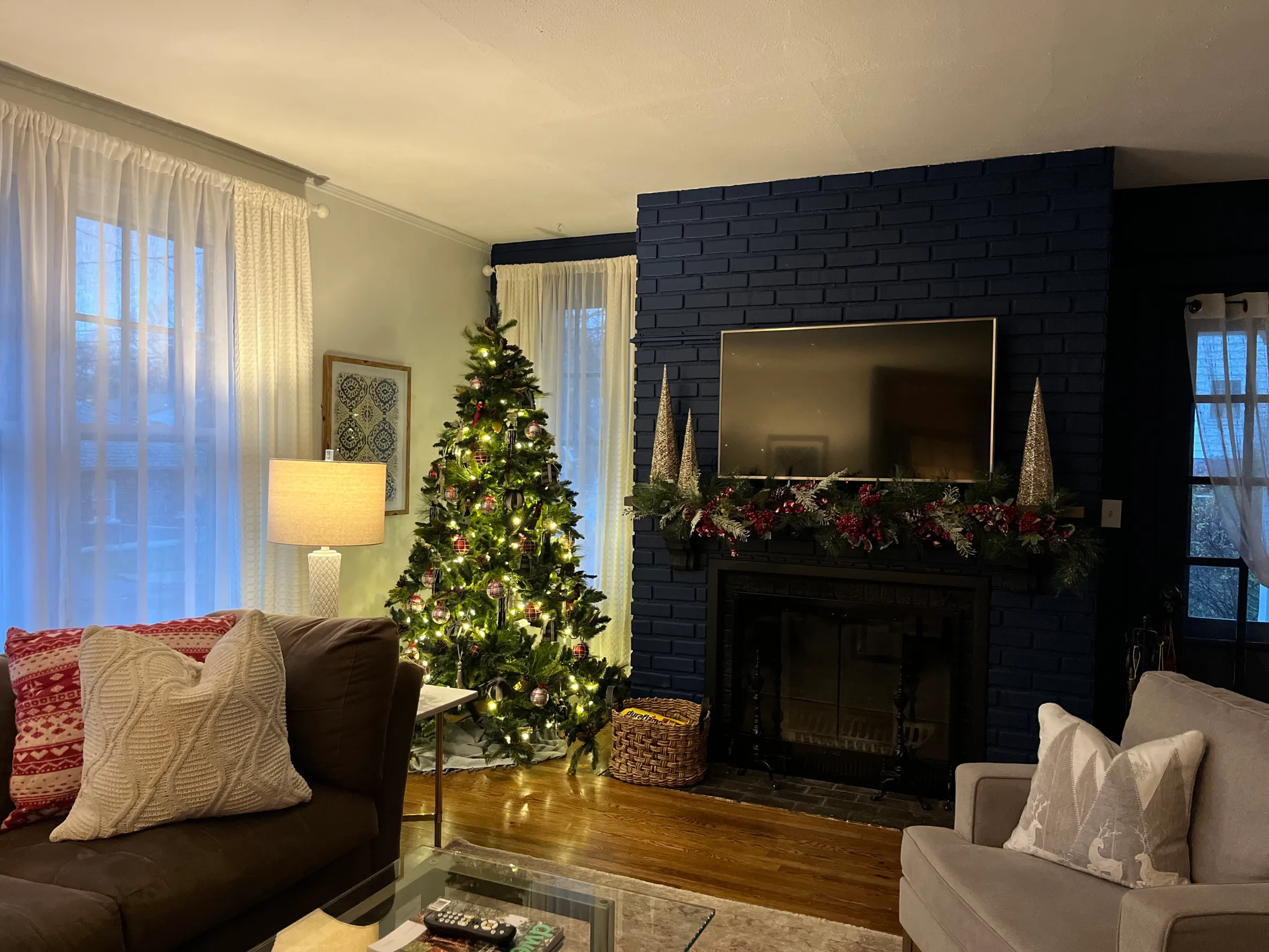 Well-lit room with a green Christmas tree with lights, a curtain-covered window, a red couch and a brown dresser