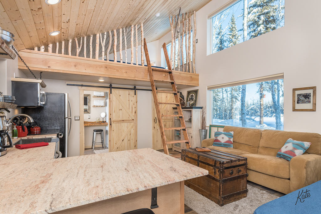 Brightly lit living room with a table, couch and window views of a snowy forrest