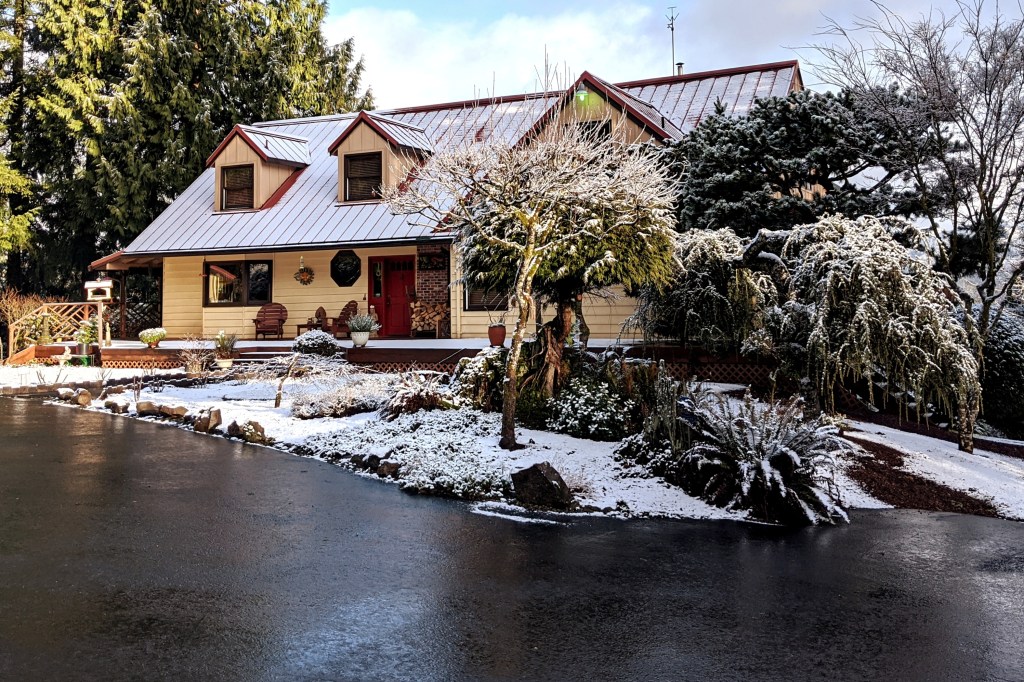 Snow covered two story home with an asphalt driiveway and a snow covered tree in front