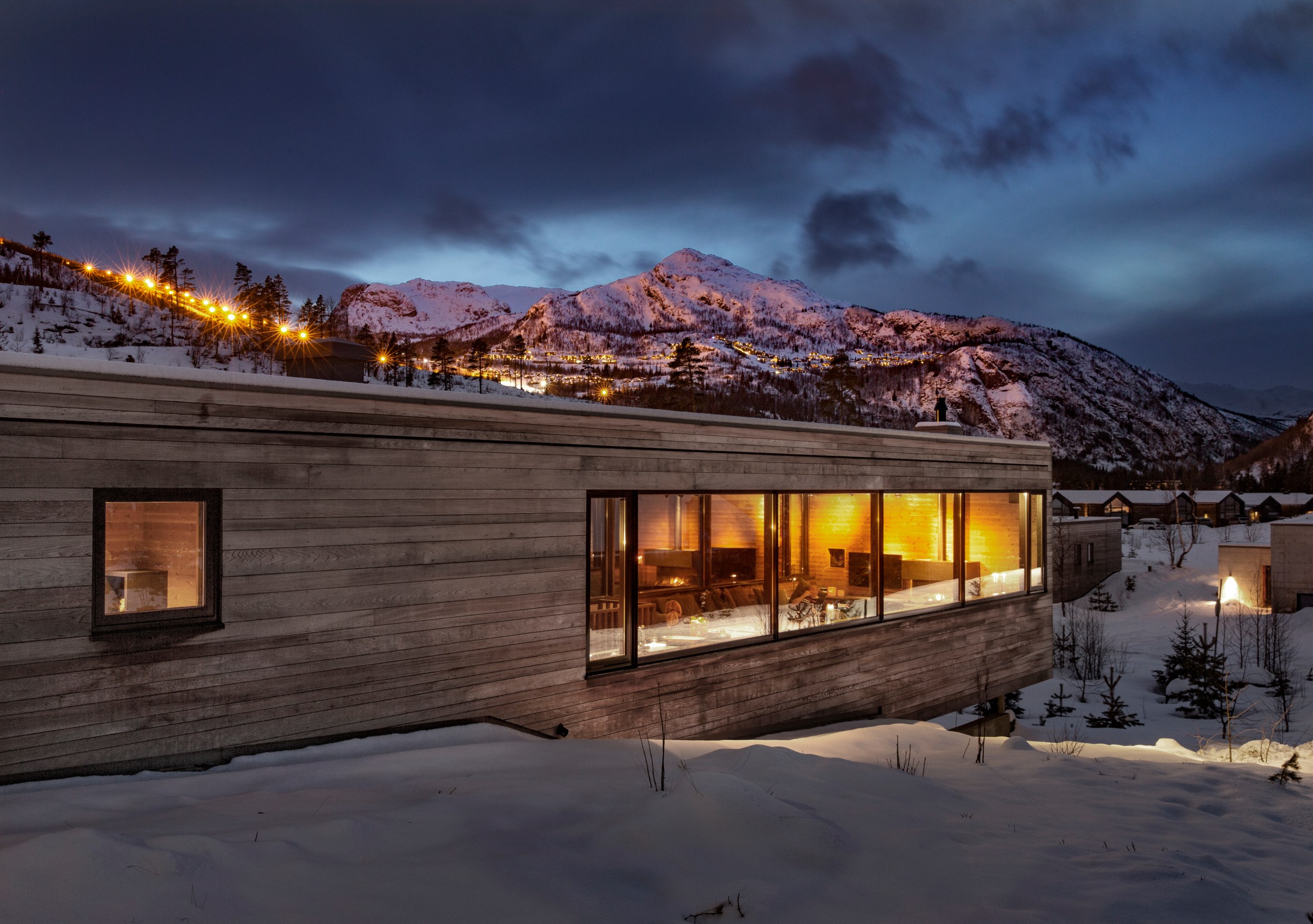 A modern cabin, set in the middle of a mountain range with large windows overlooking the views.