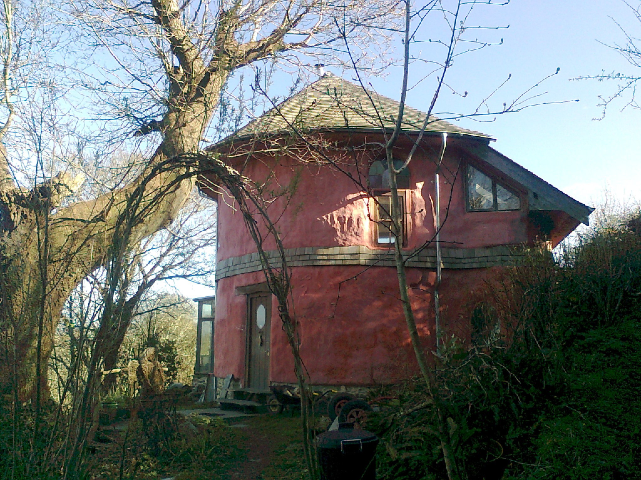 Rachel's sustainable Eco House St. Dogmaels Pembrokeshire is a cylindrically shaped building painted a clay red.