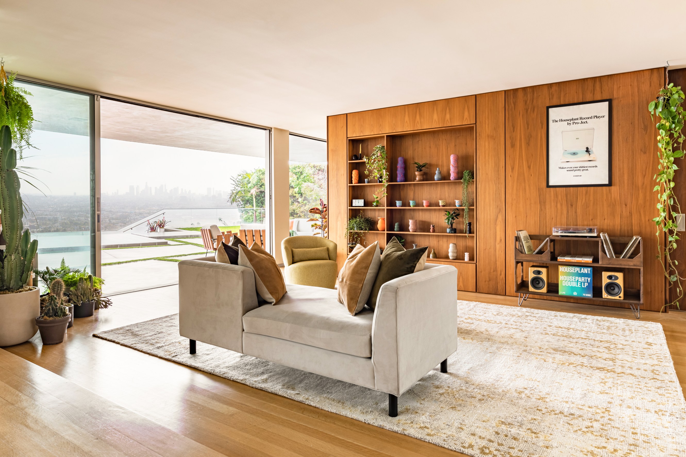 Houseplant home living room, which includes floor to ceiling windows with a view of downtown Los Angeles, furniture, plants, a record player, and a pottery wall.