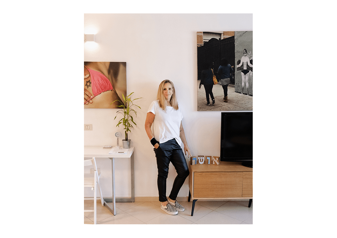 woman standing in her living room against a white wall decorated with art. 