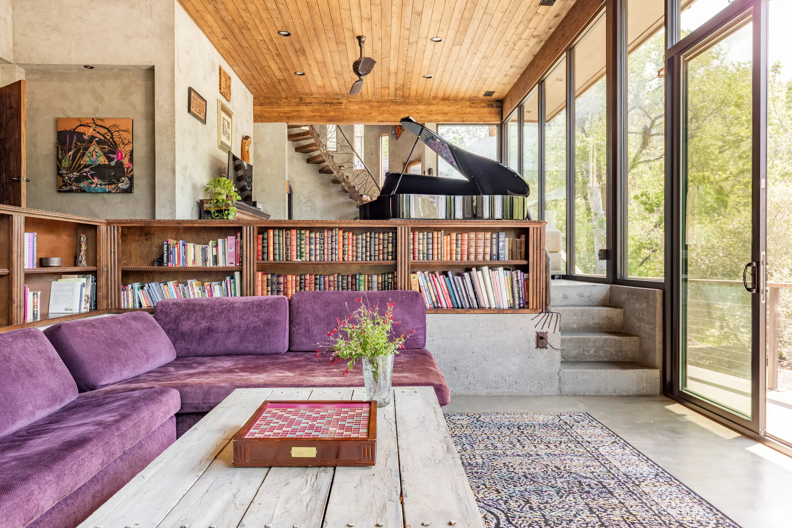 living room with couches, piano, books on shelves and floor to ceiling windows