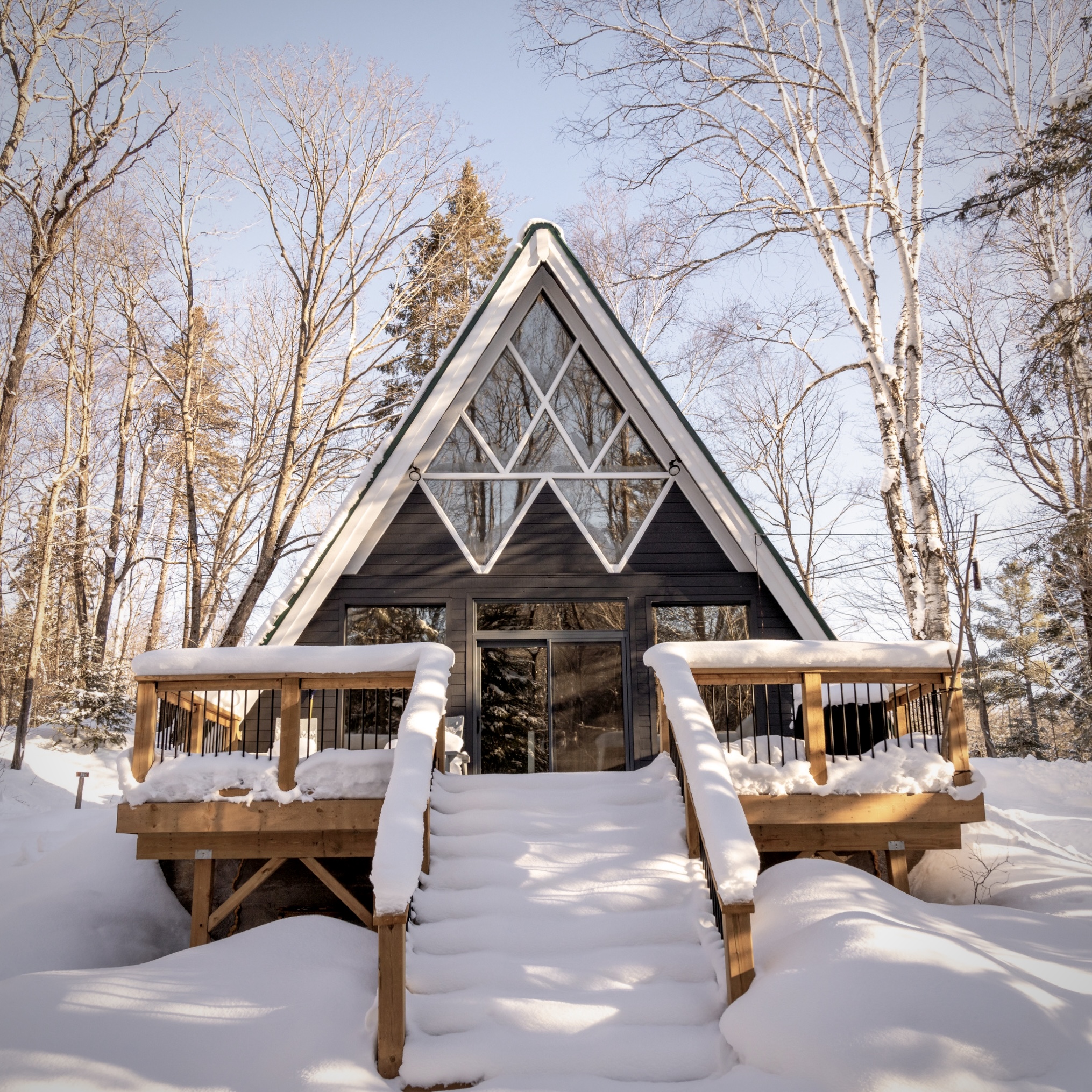 Snow capped A-frame cabin with a snow covered porch and front staircase. 