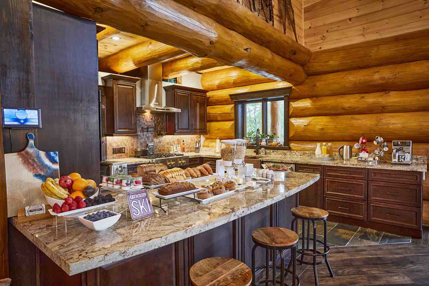 A lavish breakfast spread on a granite countertop in a rustic but modern Swiss-inspired log-walled kitchen. 
