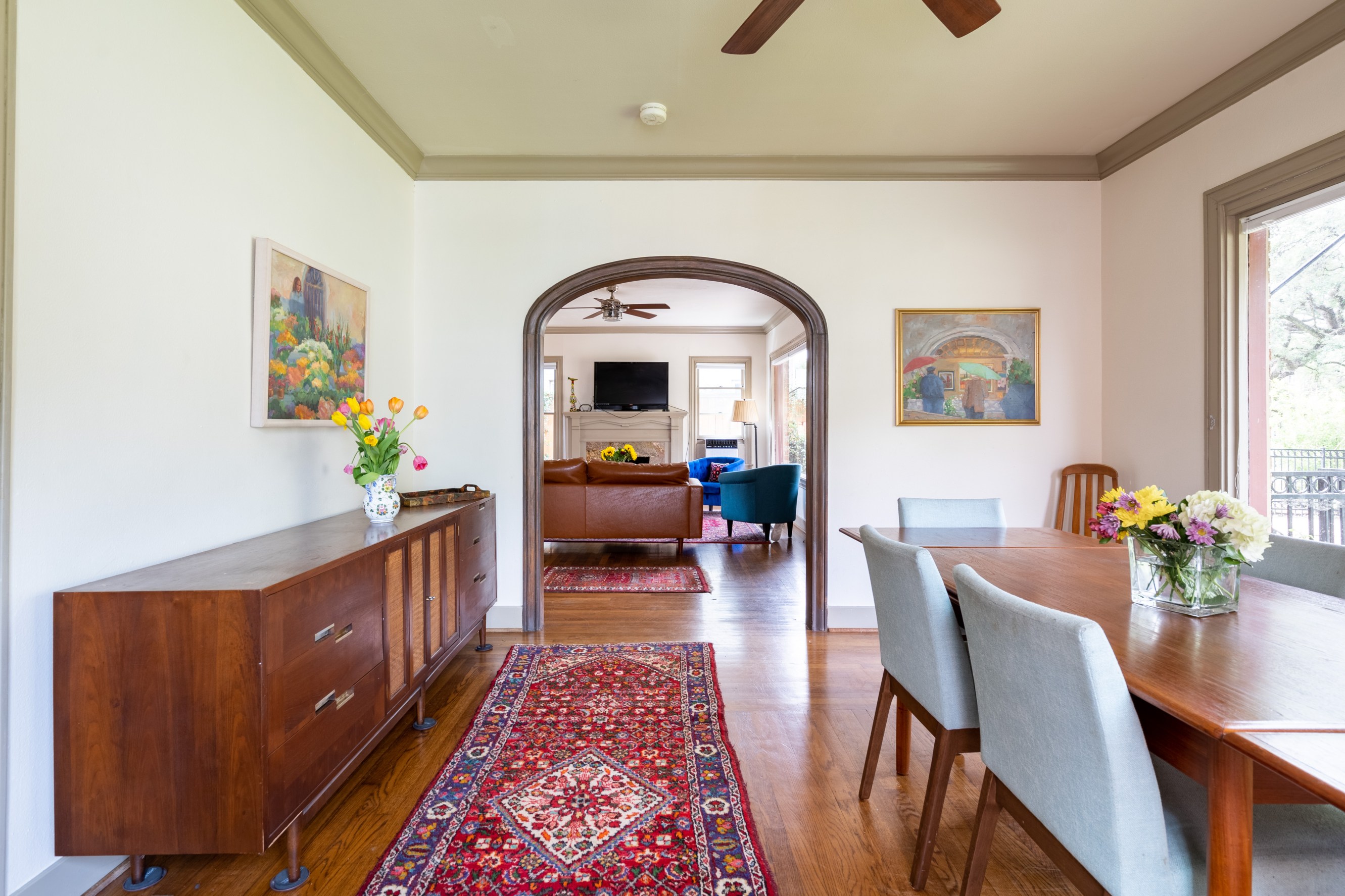 A bright and open dining room with a wooden antique credenza, an imperial runner carpet and a dining table with seating on the right.