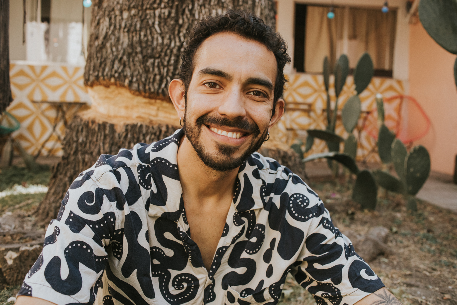 Stefano, anfitrion de Airbnb con camisa de estampado blanco con negro, sonriendo, al fondo algunas plantas y el tronco de un arbol