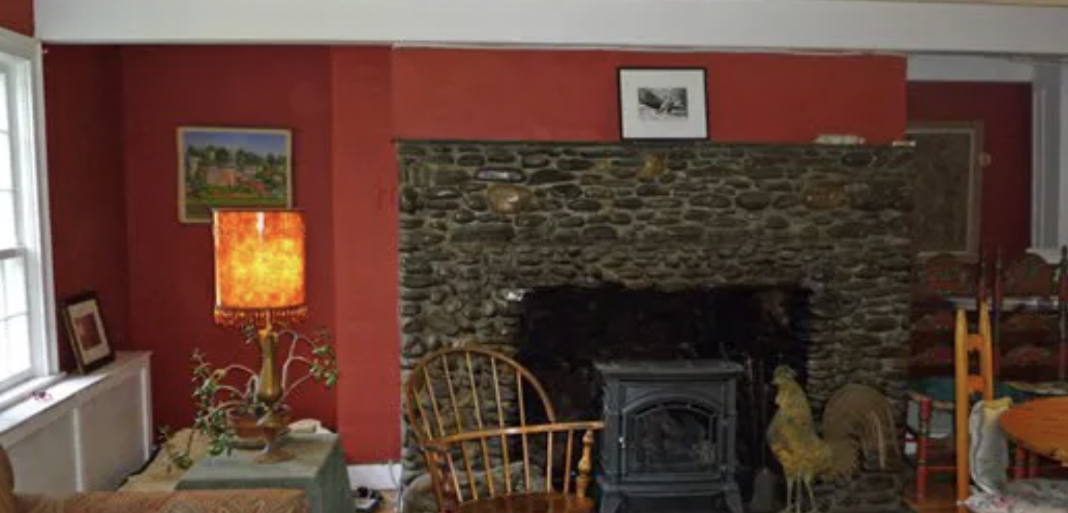 More recent image of The Pond House pre-renovation, showing a red painted living room with a cobblestone fireplace.