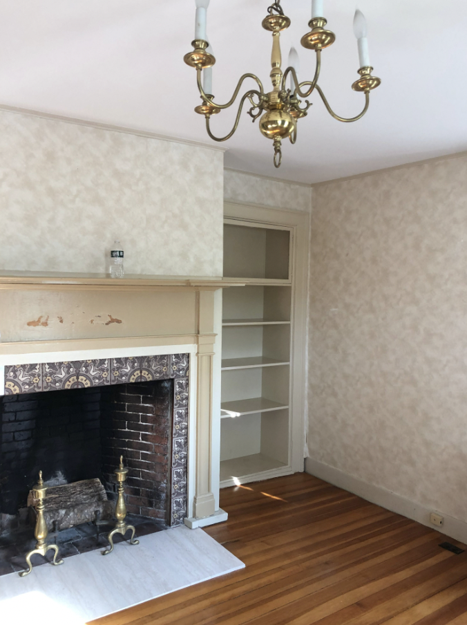 Old, empty living room with wallpaper, a fireplace and bookshelf.
