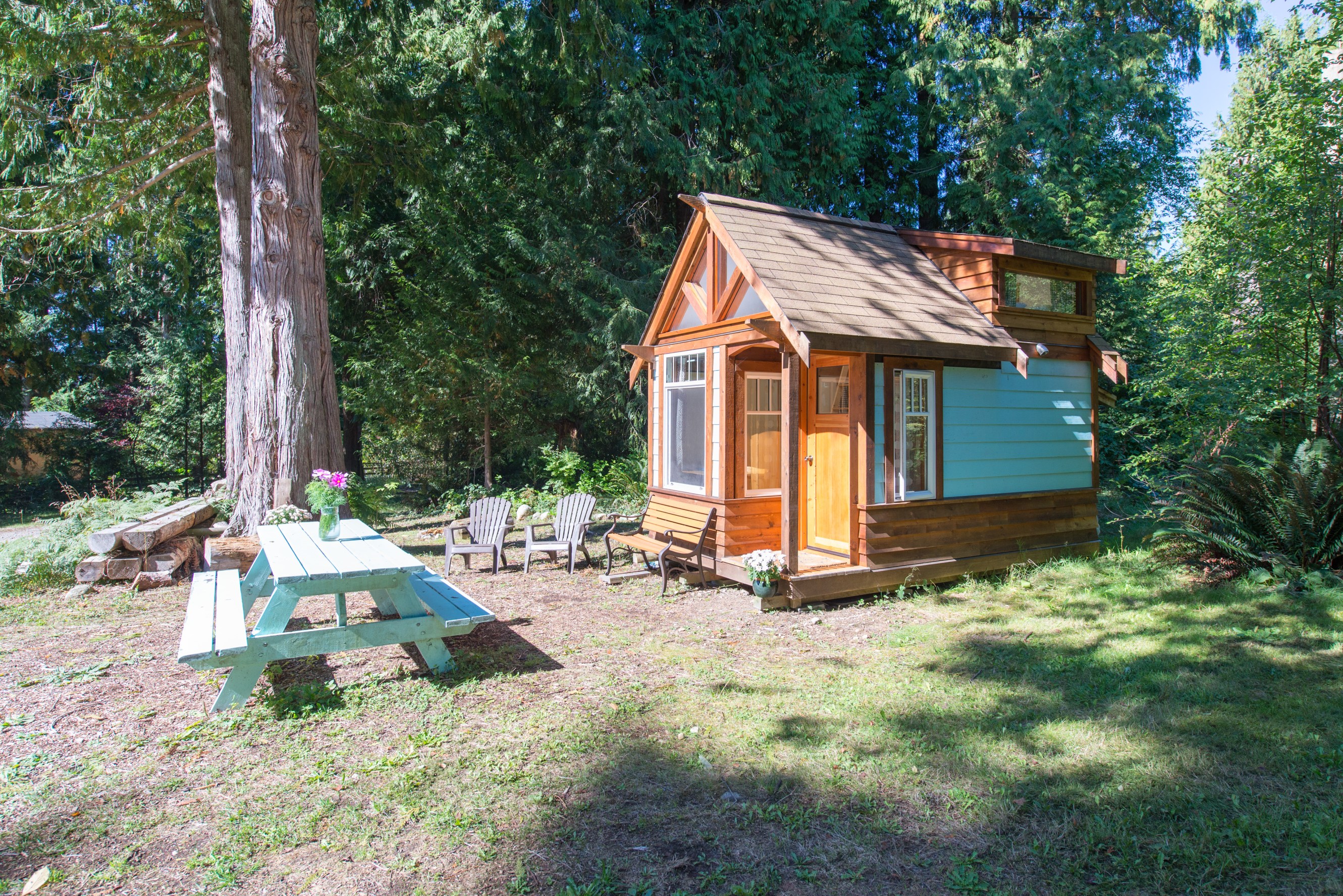 A mini cabin with a picnic table and chairs in the forest. 