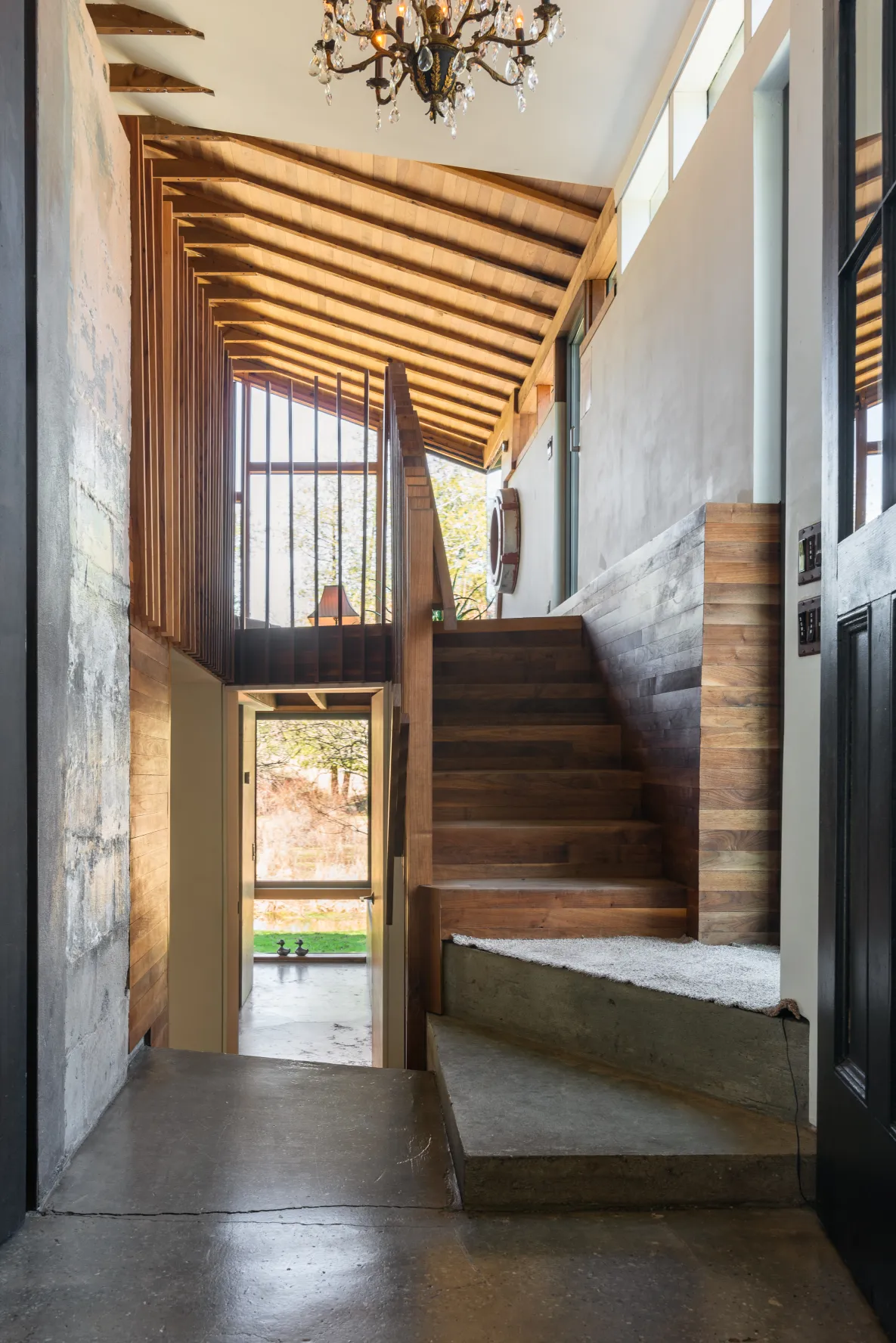 Interior shot of The Pond House post-renovation, showing an airy and modern hallway with wooden steps and an exposed beam ceiling.
