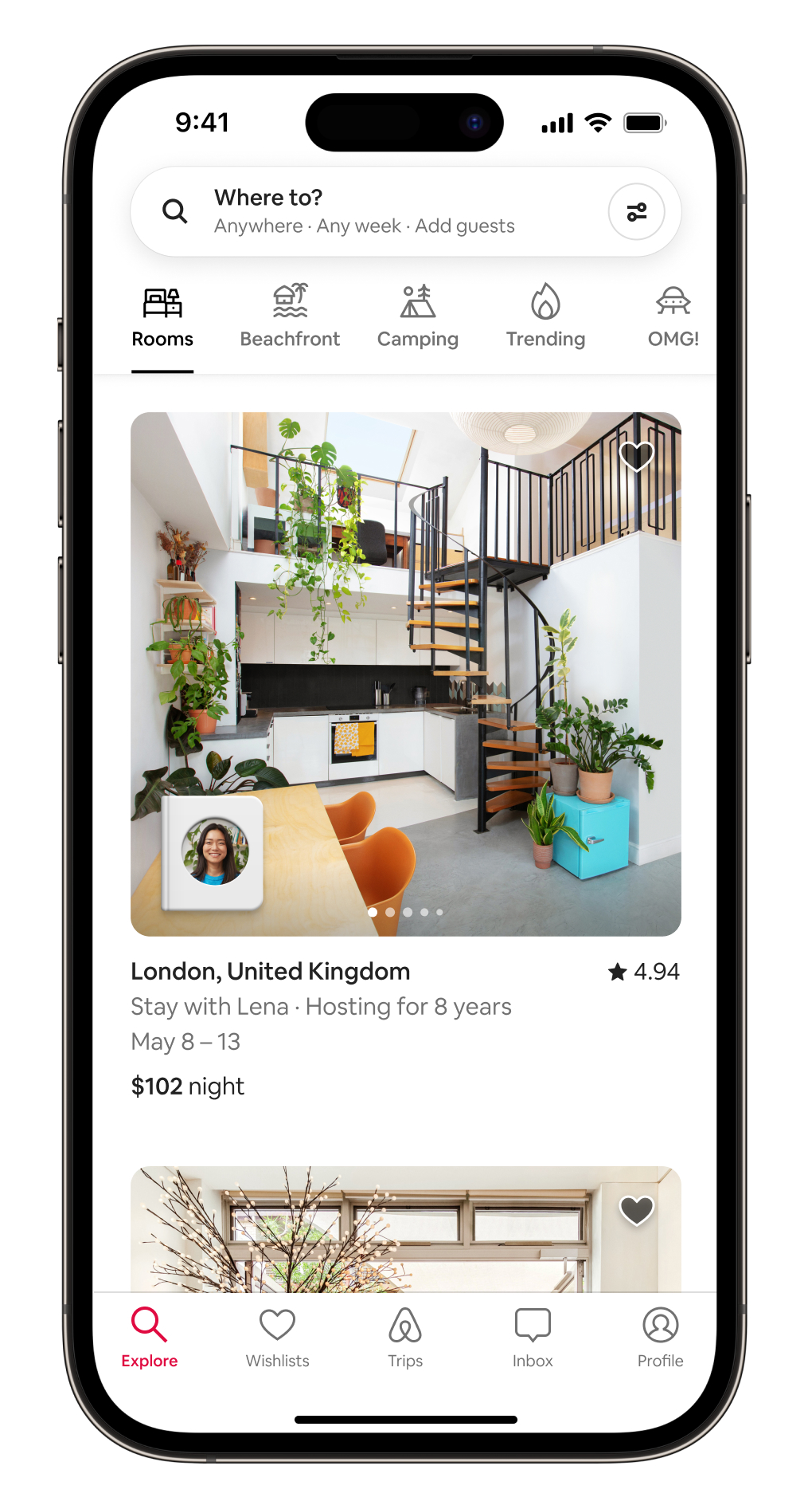 iPhone screen showing a view of the Airbnb app, which displays the new Rooms category, including an interior photo of a stay with all white walls, some hanging plants and a spiral staircase leading from the first floor kitchen to a lofted area.