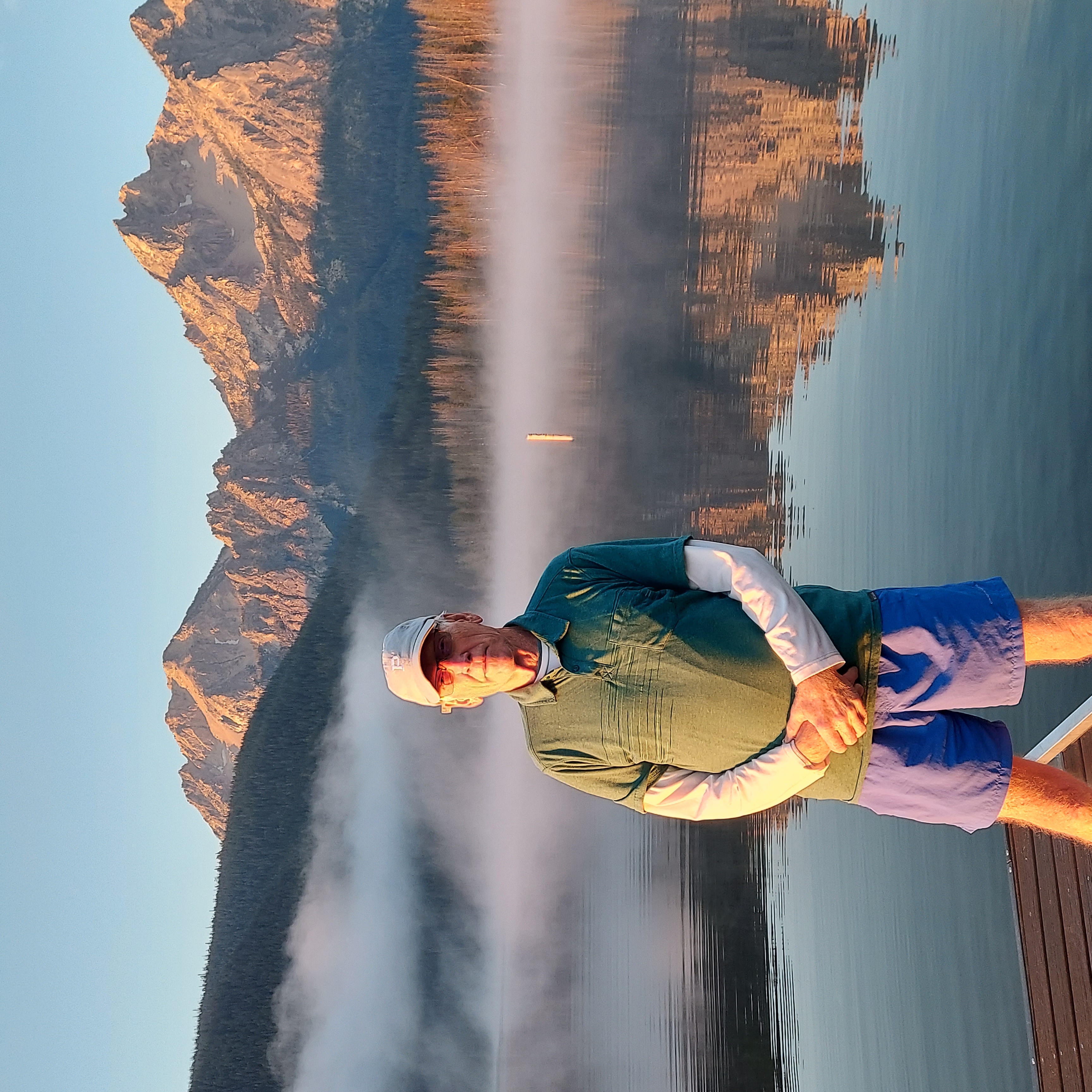 Man standing in front of lake and mountains. 