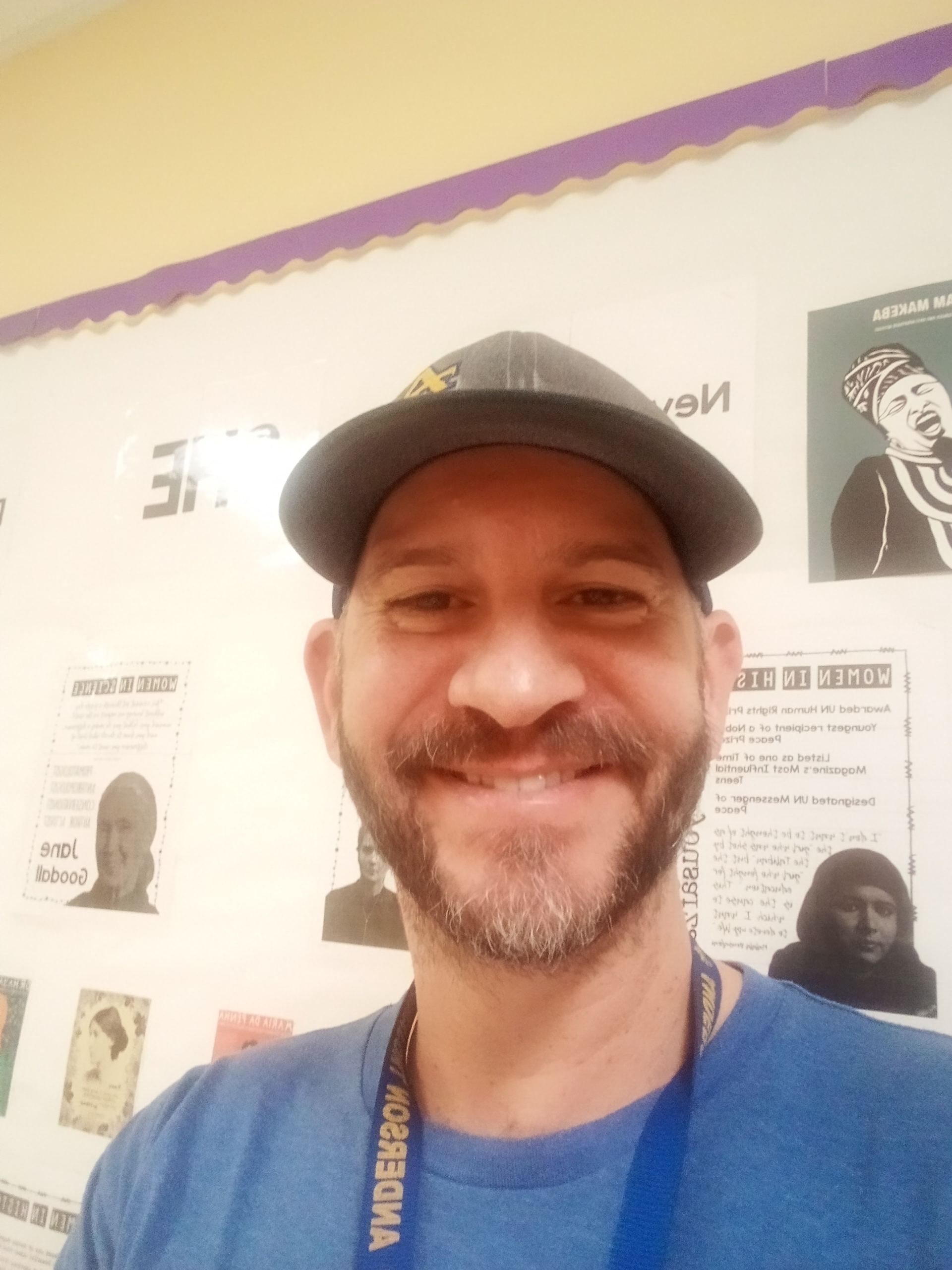 Man smiling for a selfie in front of a whiteboard in a classroom. 