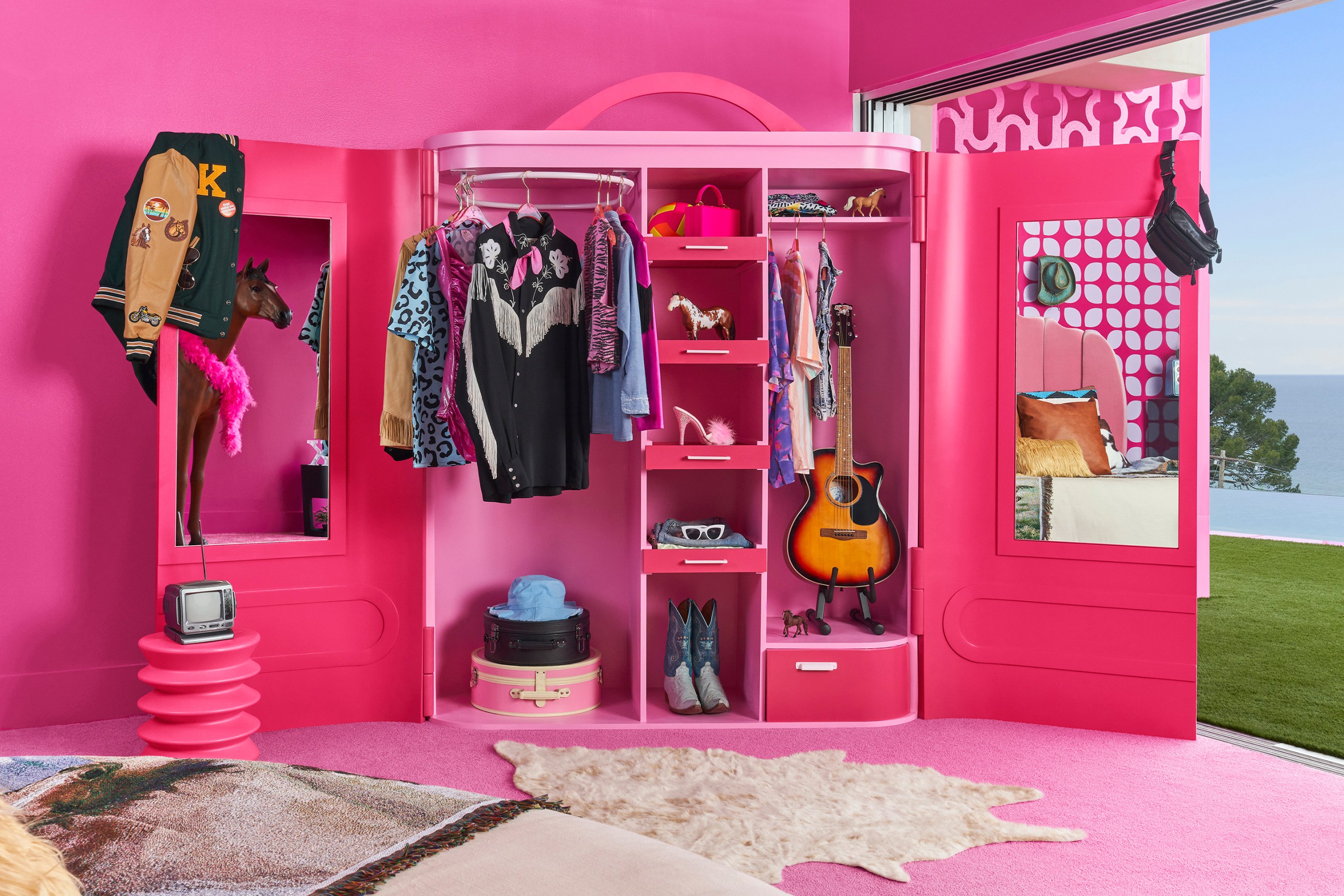 Interior of Ken's closet, bright pink, styled with jackets, shirts, a fanny pack and a guitar.