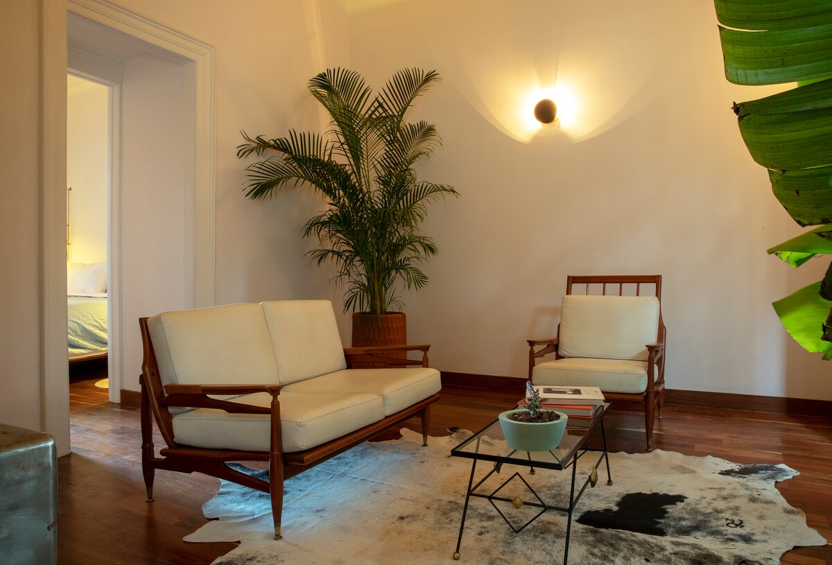A sitting room with two white chairs and a palm tree in the corner. 