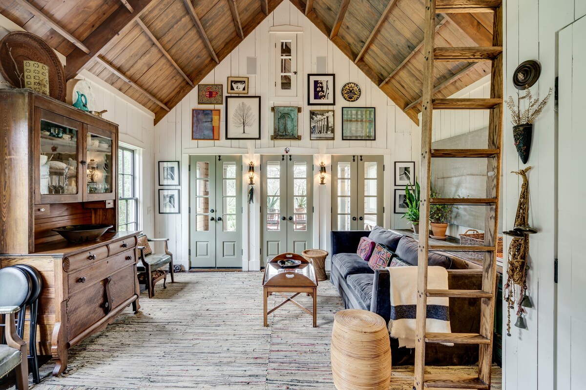 A sitting room with a wooden thatched roof, pictures on the walls and a wooden ladder leading up to the attic. 