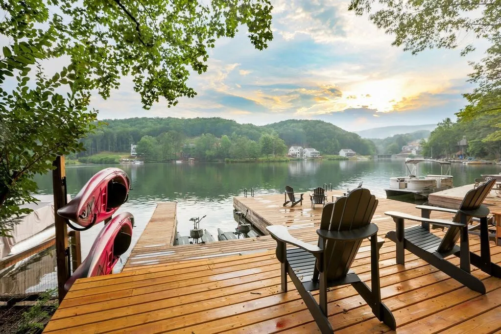A wooden deck with two chairs looking out to the view of a lake. 