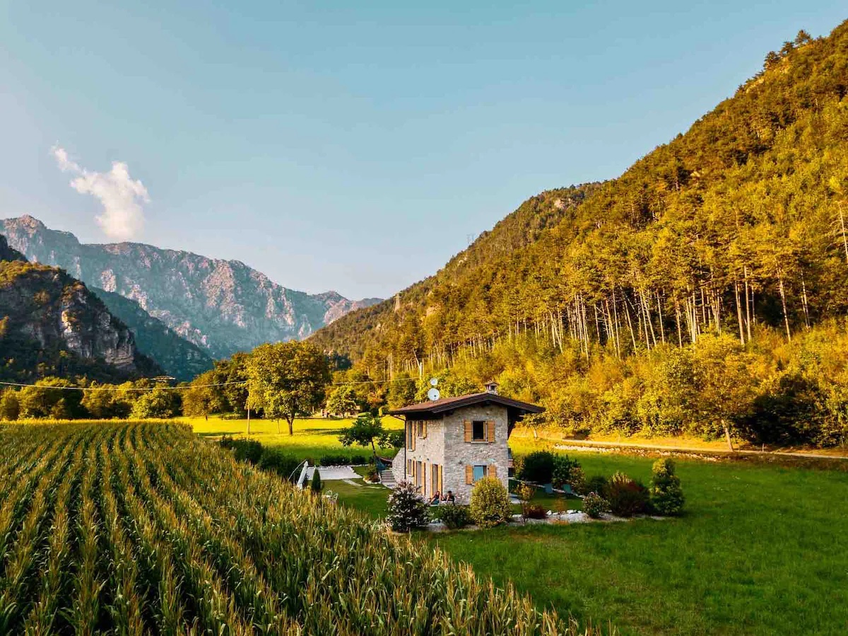 Picture of a large villa in the middle of fields and trees and mountains in the background. 