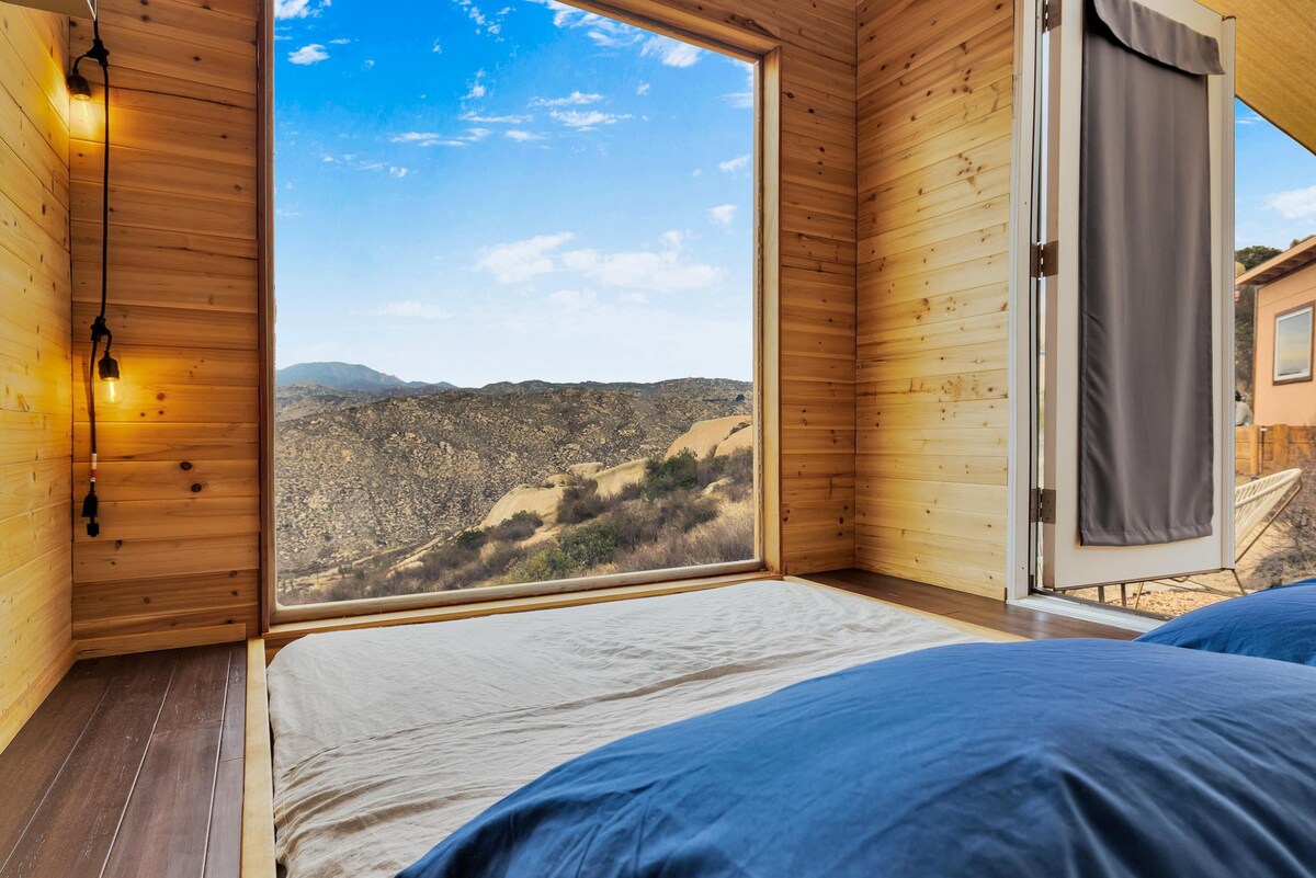 Large window in a timber cabin showing the view of rocky mountains.