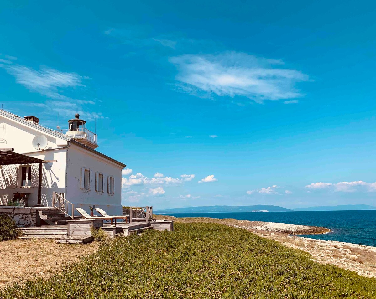 White lighthouse sits alongside an ocean coastline