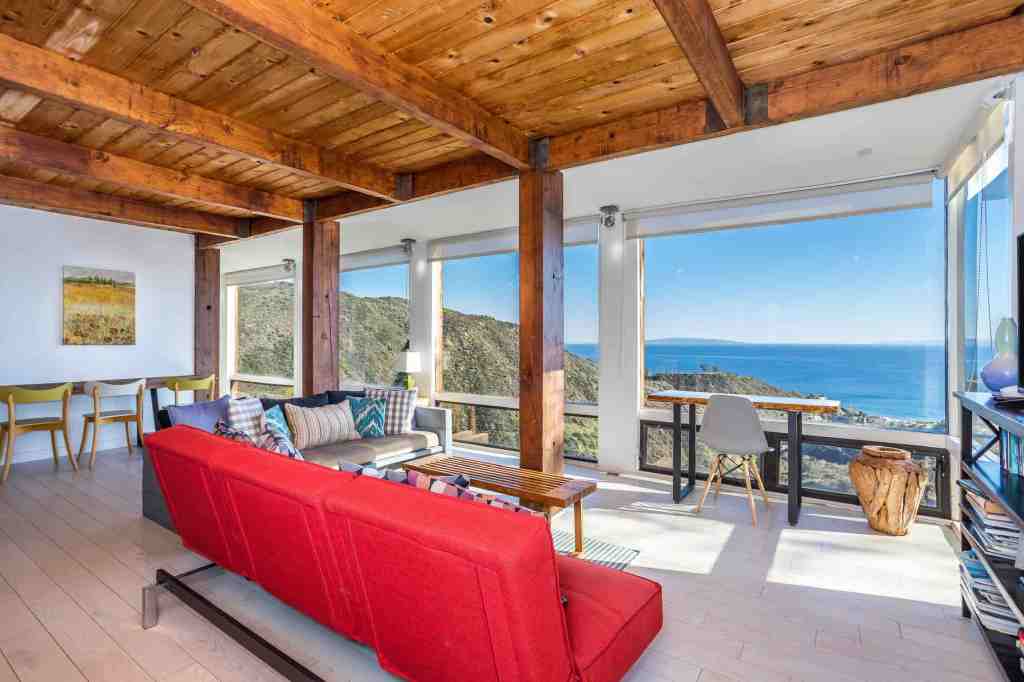 Living room with red couch and floor to ceiling windows showing the Malibu coastline