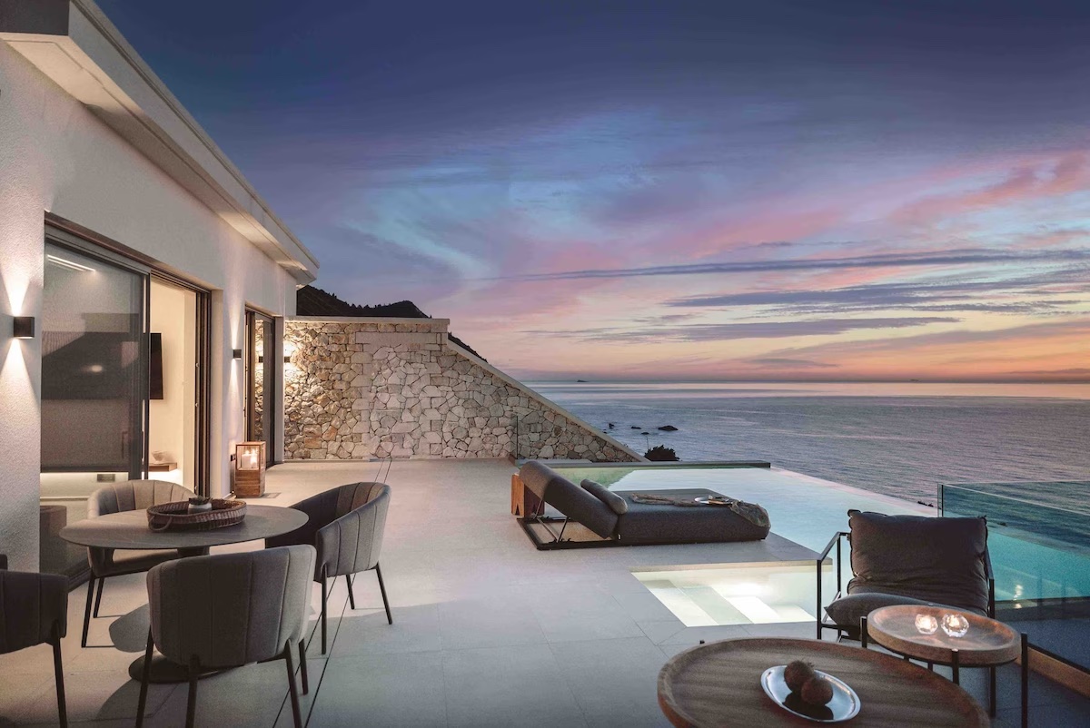 A contemporary outdoor patio with a dining set, lounge chairs and an infinity pool overlooking a sea view and sunset