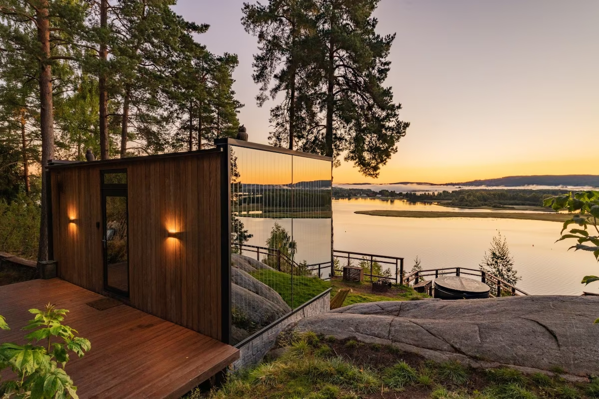 Modern cabin with floor to ceiling windows sits along a quite lakeside corner