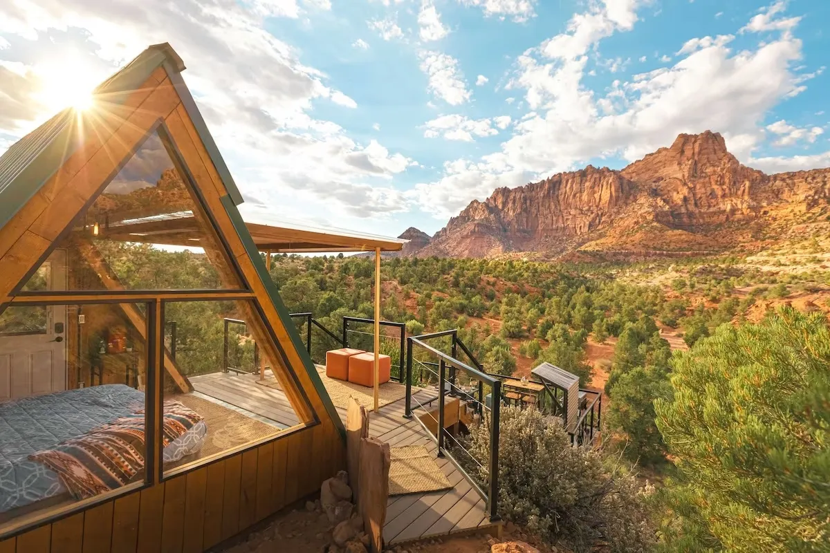 A-frame wooden cabin with floor-to-ceiling bedroom windows overlooks a red rock canyon