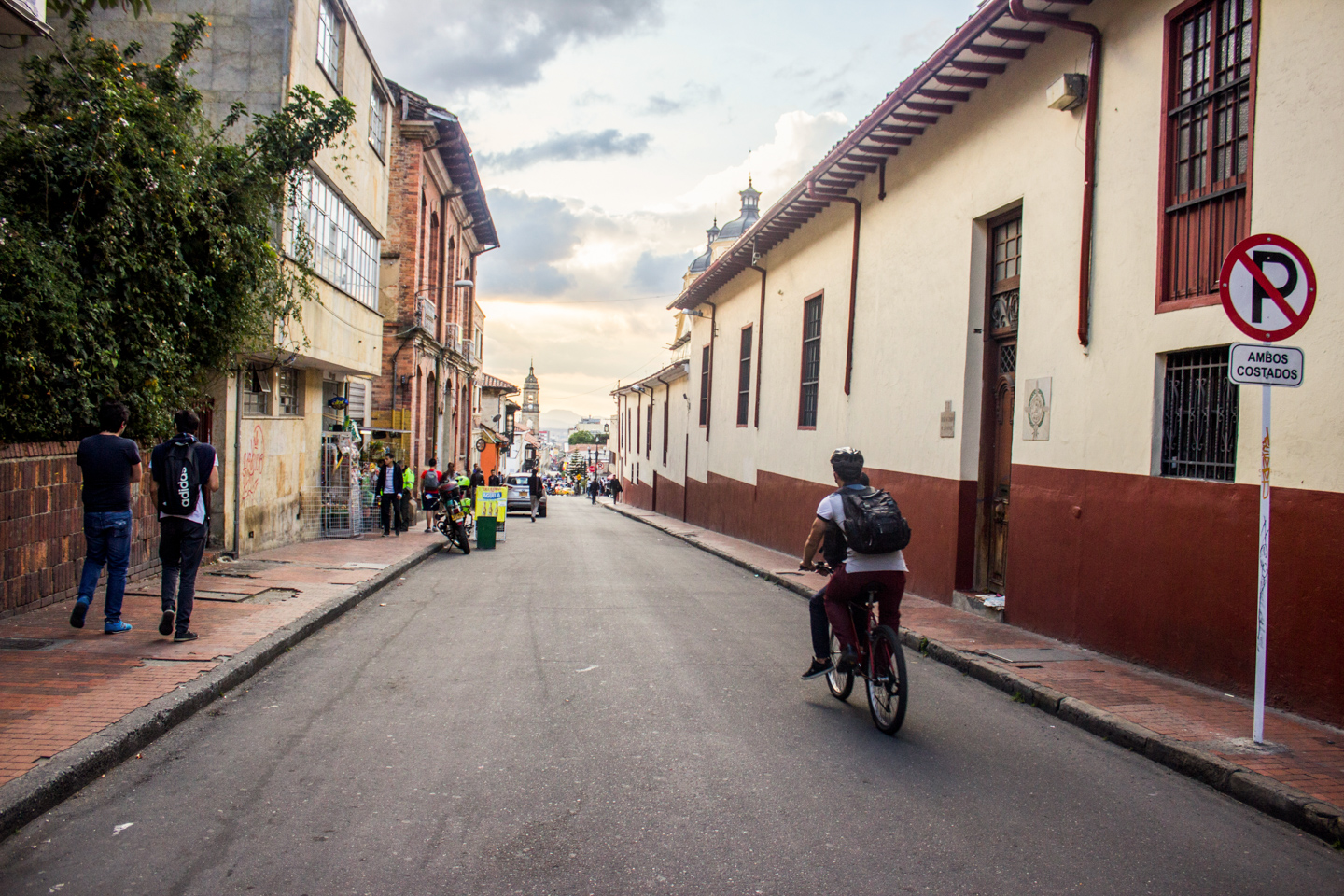 Hombre montando motocicleta en el costado derecho de una calle de La Candelaria, Bogotá, Colombia