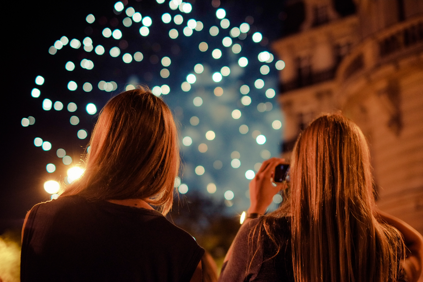 Dos mujeres de espalda ven juegos artificiales en un cielo oscuro