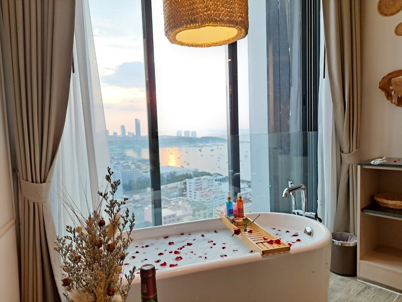 A bathtub  filled with rose petals with city views and water in the background