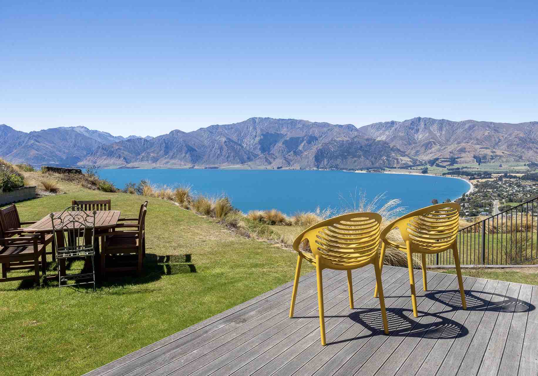 A patio and grass backyard overlooking a lake view with mountains