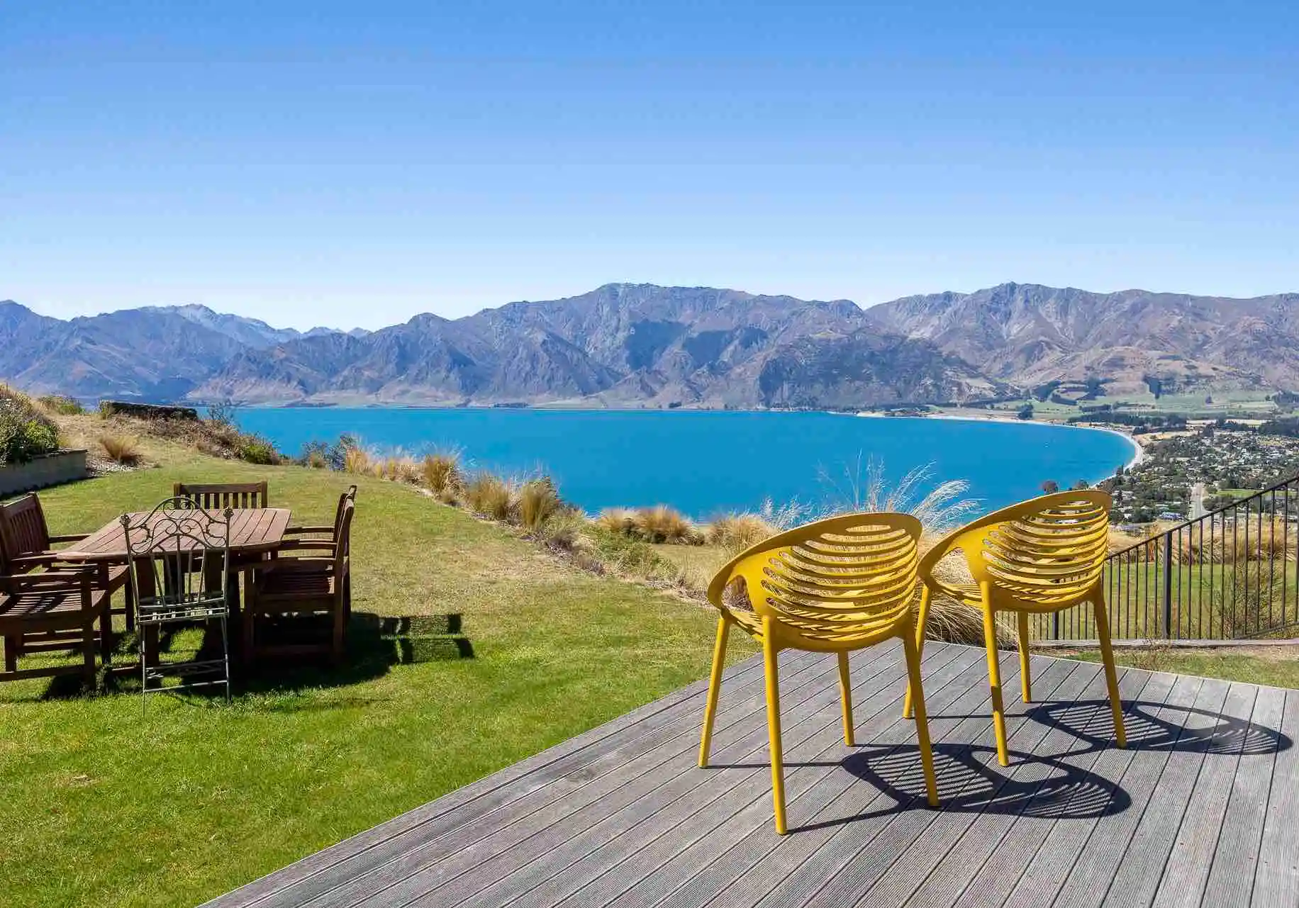 A patio and grass backyard overlooking a lake view with mountains